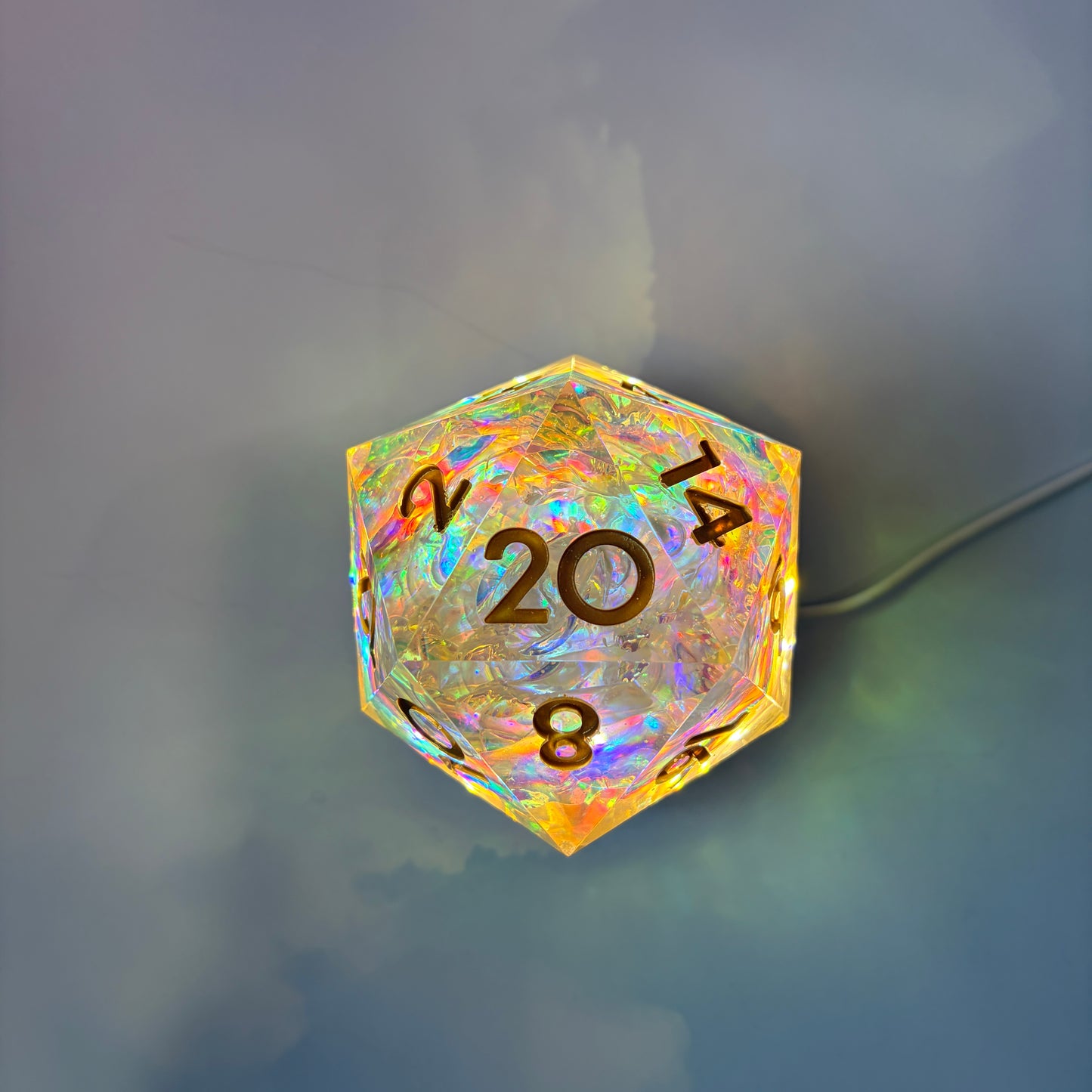 Large resin D20 with gold numbers on illuminated wooden base.