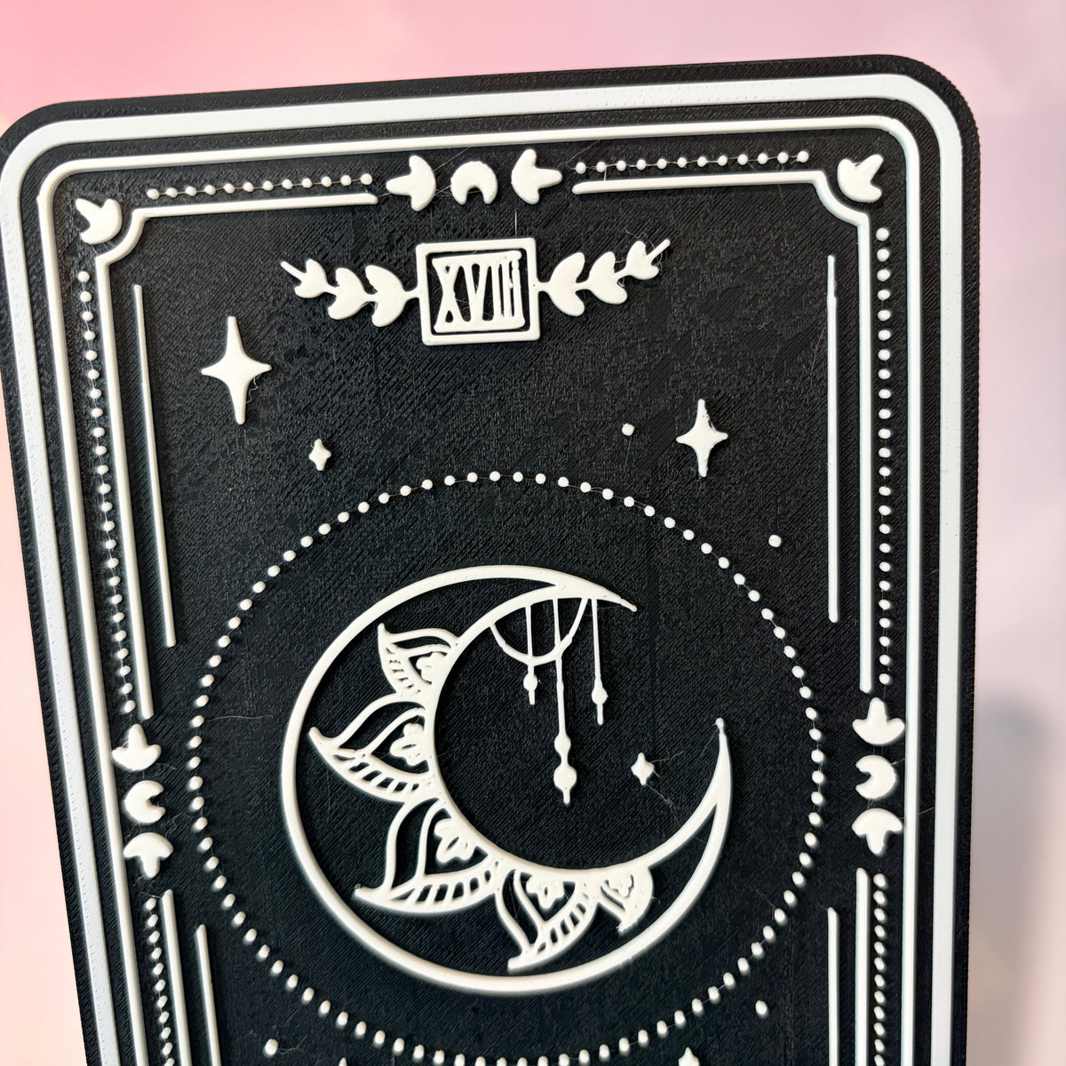 A vertical 3D printed tarot card sign featuring The Moon from the Major Arcana, displayed upright on a small black easel against a soft pink, peach, and lavender background. All 22 Major Arcana tarot card designs are available, allowing customers to choose a card that reflects their interests, spiritual practice, or personal journey.