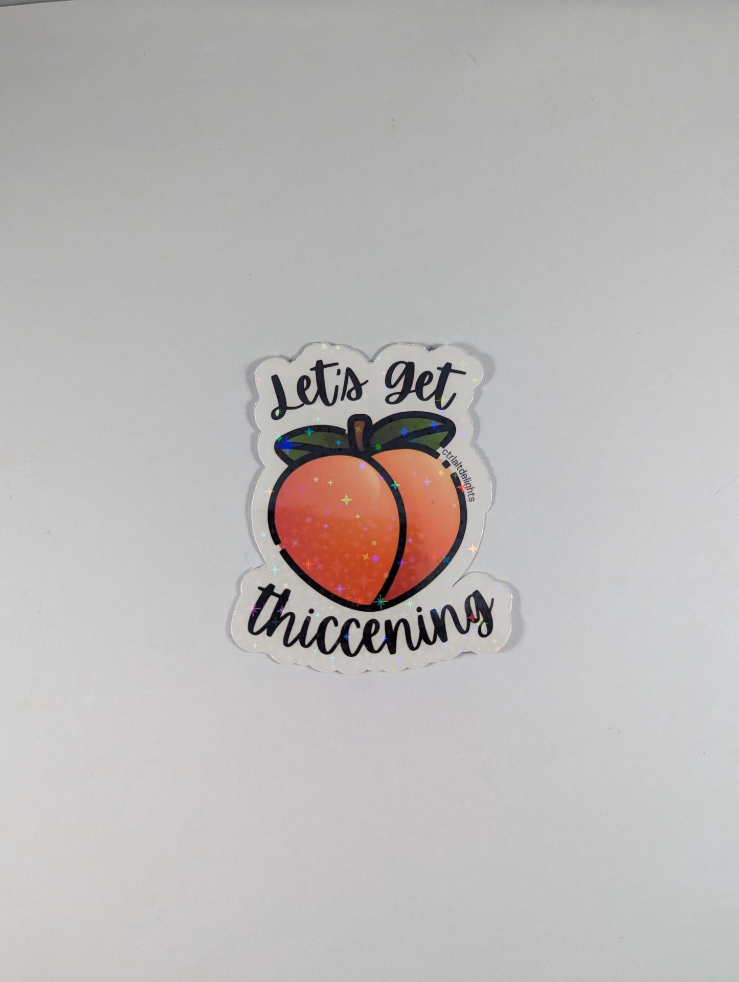 Holographic "Let's Get Thiccening" peach sticker featuring a cute peach design. Perfect for decorating water bottles, laptops, journals, or any surface that needs a fun, thicc touch.
