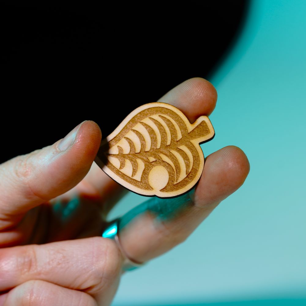 Laser engraved wood pin shaped like the Animal Crossing leaf, perfect gamer gift or accessory for backpacks, jackets, or collectors of gaming-themed items.