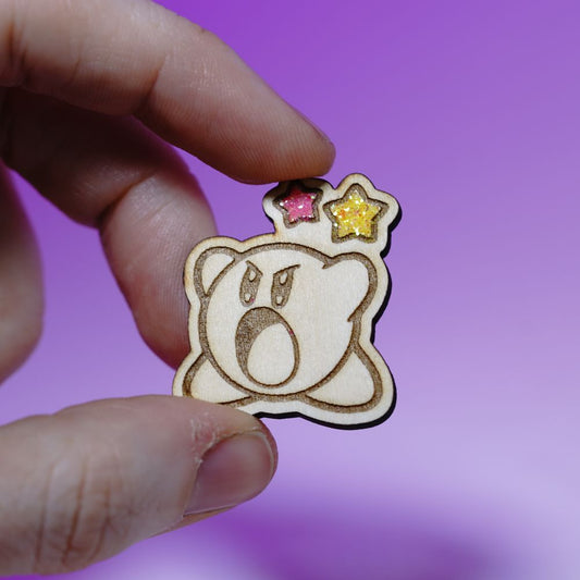 Cute Kirby wood pin with laser engraving and glittery star accents. Handmade gamer brooch for Nintendo fans, perfect for jackets or bags.