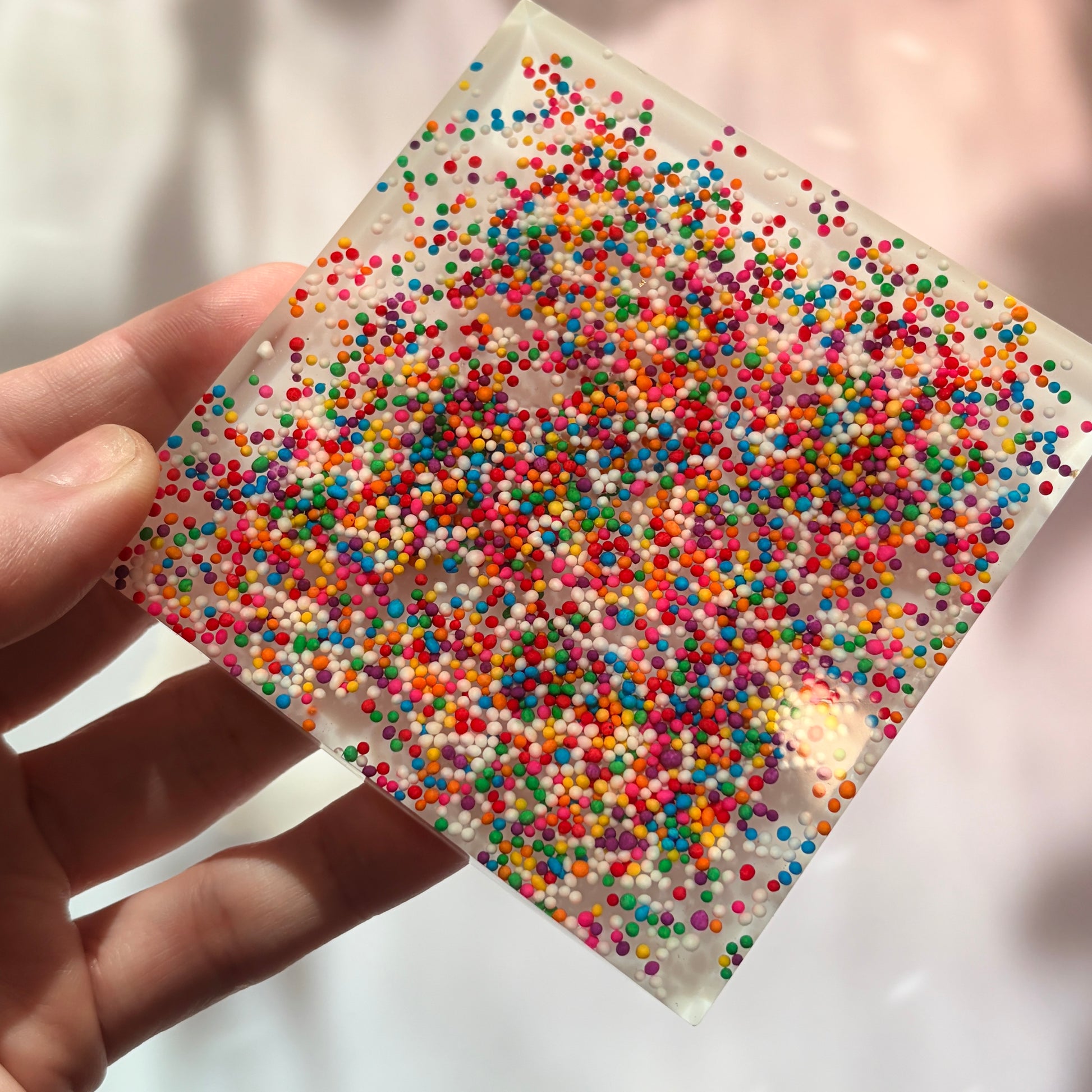 Resin coaster inlaid with rainbow sprinkles and white backing.