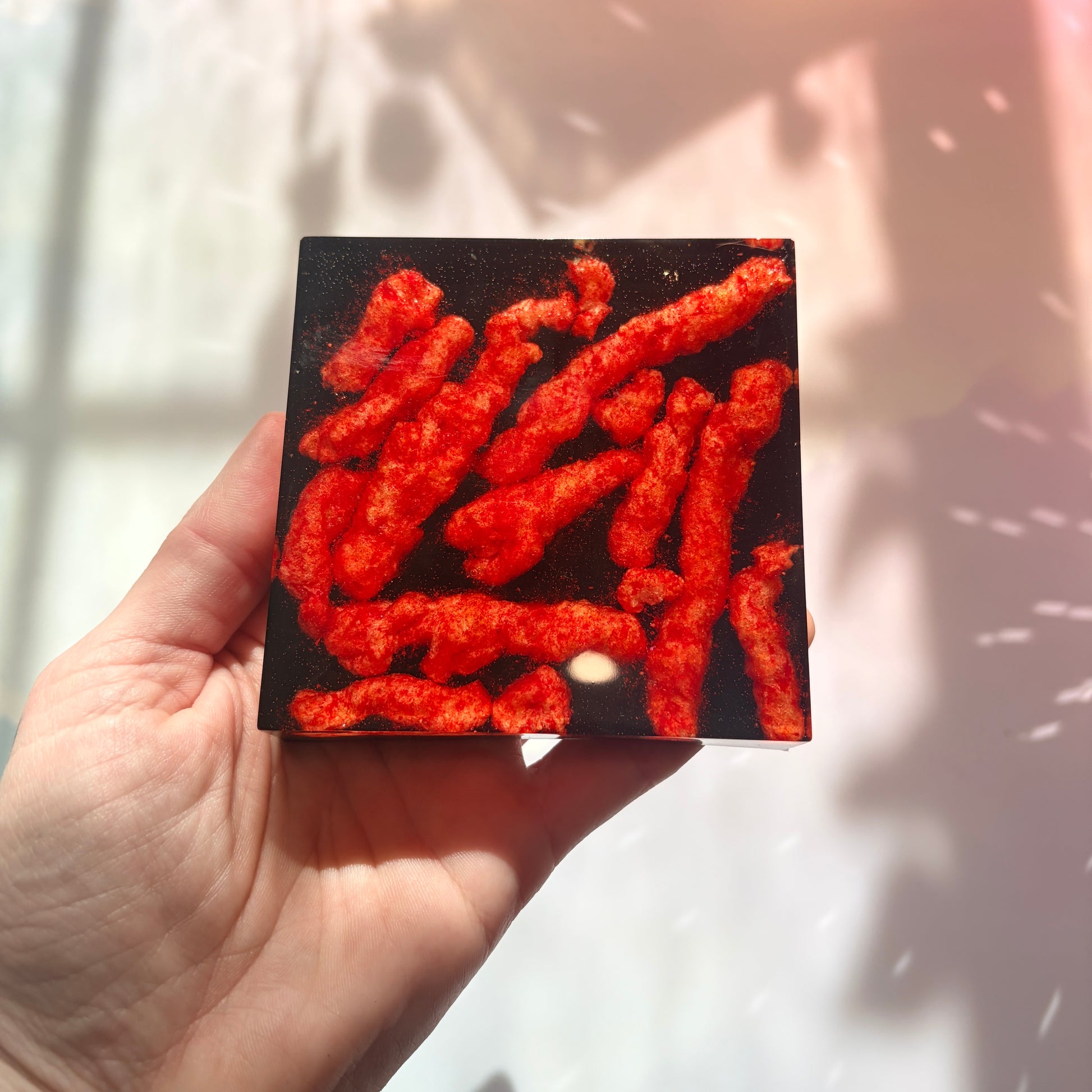 Resin coaster inlaid with Hot Cheetos and black backing.