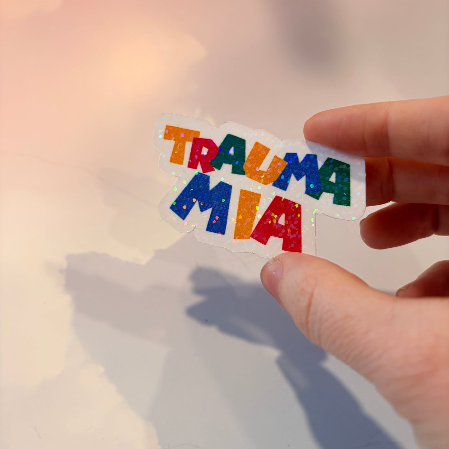Holographic Trauma Mia sticker in retro video game style lettering.