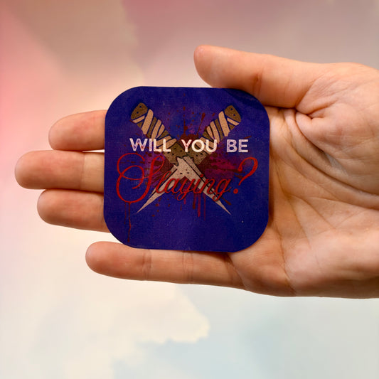 A hand holding a squarepurple sticker with rounded corners featuring a graphic of crossed stakes and the text 'WILL YOU BE Slaying?' in white and red.