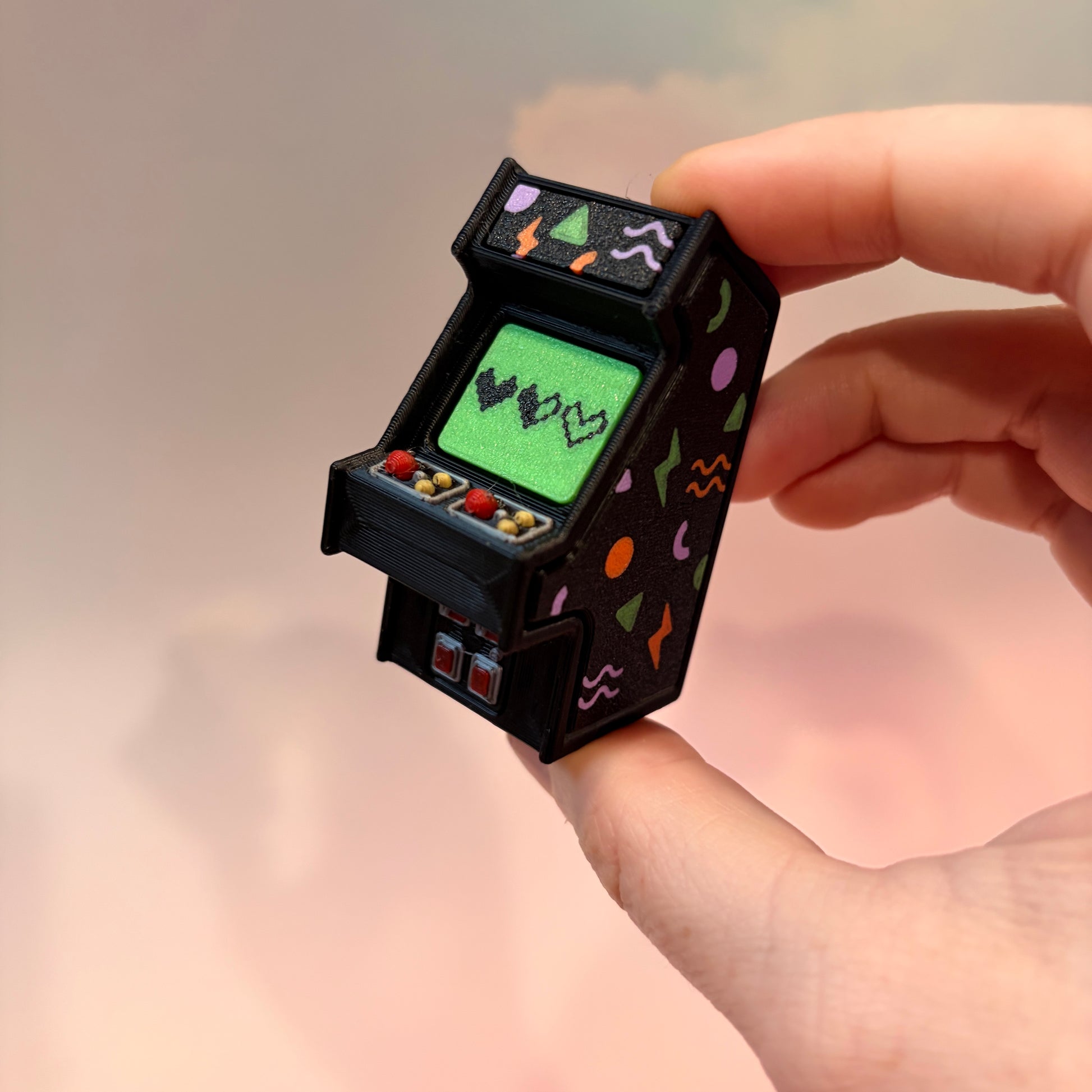 Mini retro arcade machine fidget clicker keychain with colorful 90s-inspired graphics, green screen, and 3D printed design, available in clicky or silent.