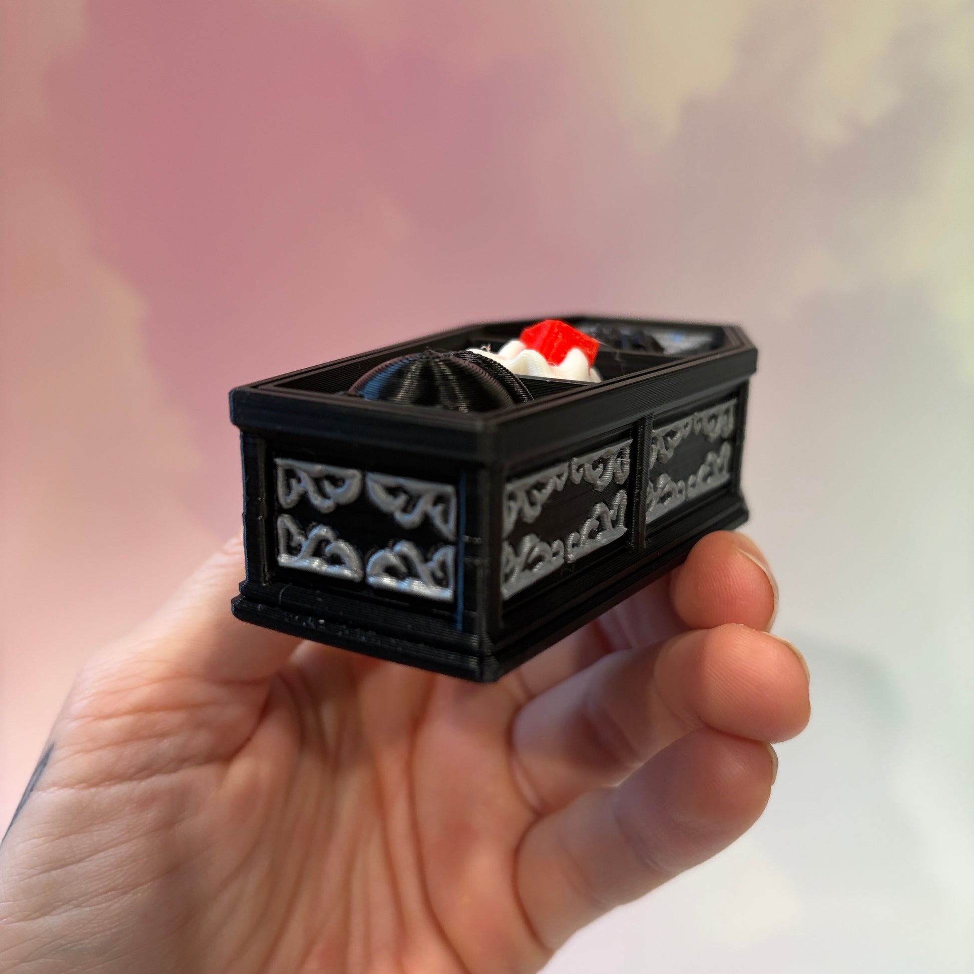 Mini 3D printed black coffin shelf fidget clicker with silver gothic trim and red interior. Features three decorative keycaps: a framed black spider, a ghost reading a book, and a bubbling green cauldron. Includes a silver keychain and is available with clicky or silent switches.
