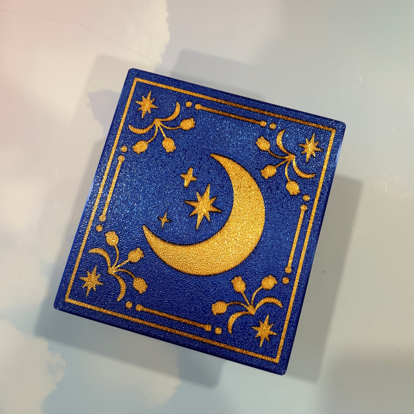 Royal blue and metallic gold 3D printed book box with a celestial moon and stars design on the cover. Opens to reveal a hidden storage compartment that holds 1–2 sets of RPG dice and doubles as a rolling tray. Perfect for jewelry, trinkets, and tabletop gaming accessories.
