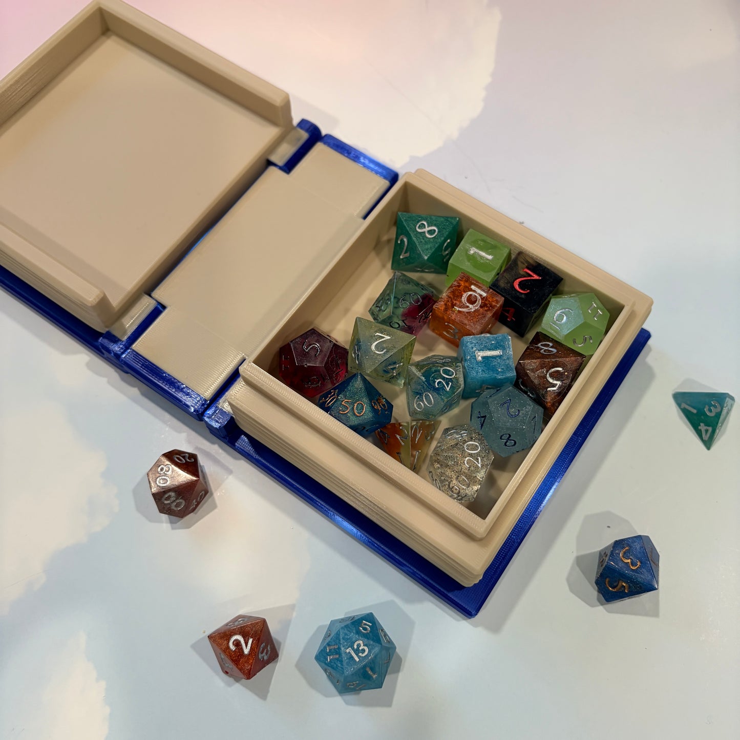 Royal blue and metallic gold 3D printed book box with a celestial moon and stars design on the cover. Opens to reveal a hidden storage compartment that holds 1–2 sets of RPG dice and doubles as a rolling tray. Perfect for jewelry, trinkets, and tabletop gaming accessories.