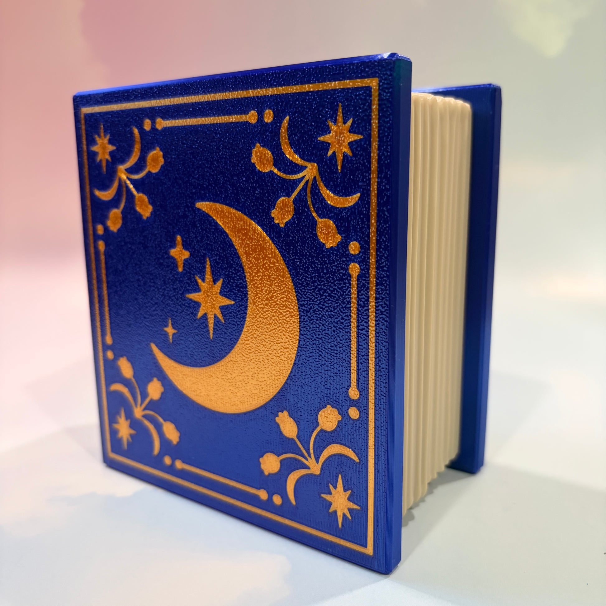 Royal blue and metallic gold 3D printed book box with a celestial moon and stars design on the cover. Opens to reveal a hidden storage compartment that holds 1–2 sets of RPG dice and doubles as a rolling tray. Perfect for jewelry, trinkets, and tabletop gaming accessories.