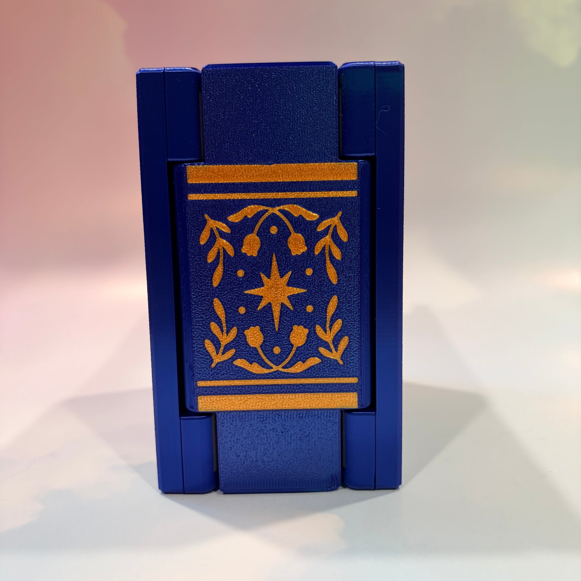 Royal blue and metallic gold 3D printed book box with a celestial moon and stars design on the cover. Opens to reveal a hidden storage compartment that holds 1–2 sets of RPG dice and doubles as a rolling tray. Perfect for jewelry, trinkets, and tabletop gaming accessories.