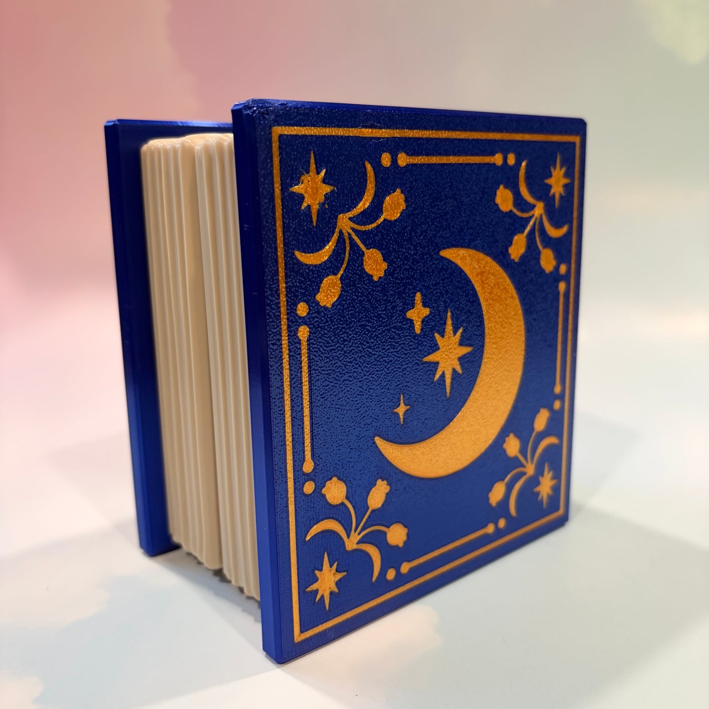 Royal blue and metallic gold 3D printed book box with a celestial moon and stars design on the cover. Opens to reveal a hidden storage compartment that holds 1–2 sets of RPG dice and doubles as a rolling tray. Perfect for jewelry, trinkets, and tabletop gaming accessories.