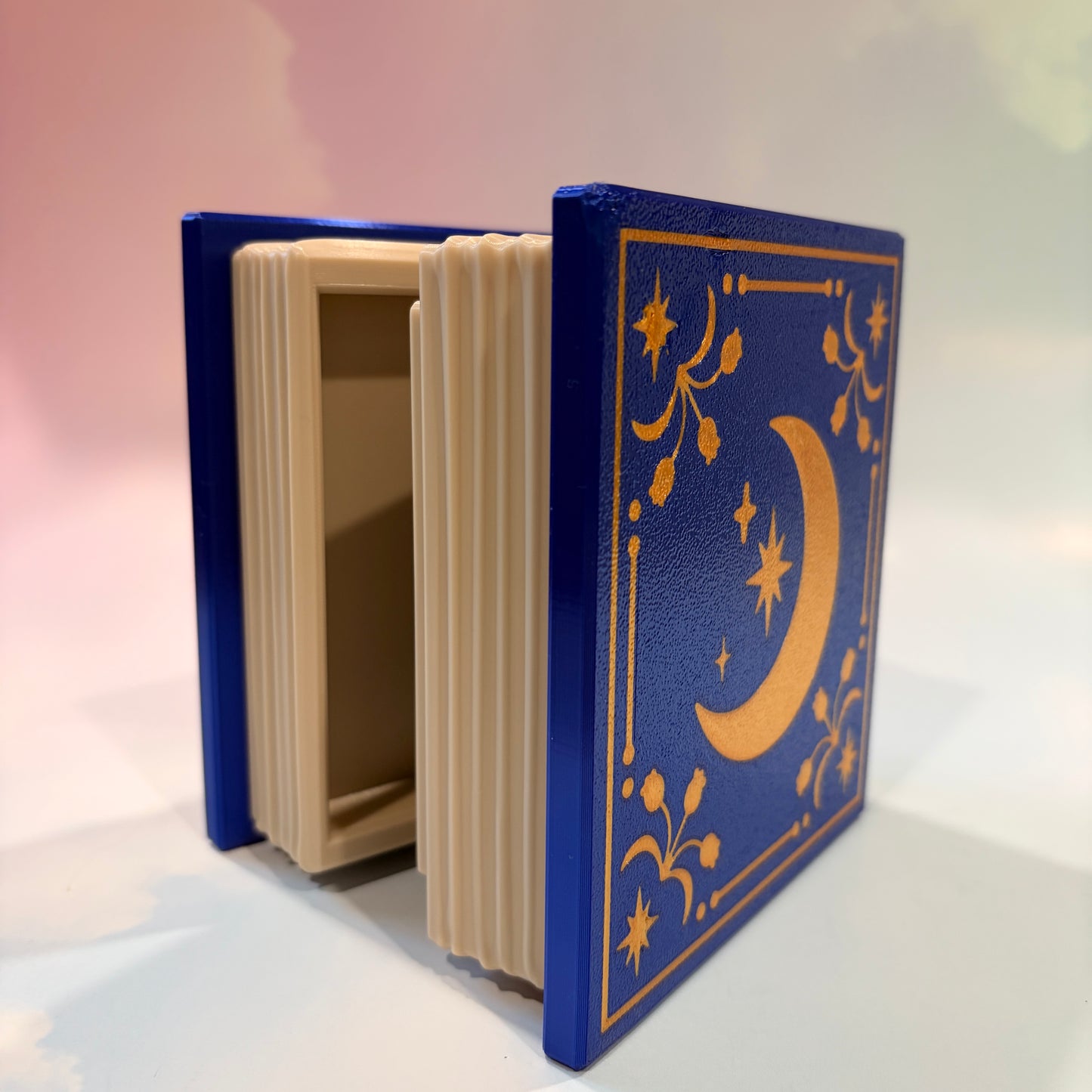 Royal blue and metallic gold 3D printed book box with a celestial moon and stars design on the cover. Opens to reveal a hidden storage compartment that holds 1–2 sets of RPG dice and doubles as a rolling tray. Perfect for jewelry, trinkets, and tabletop gaming accessories.