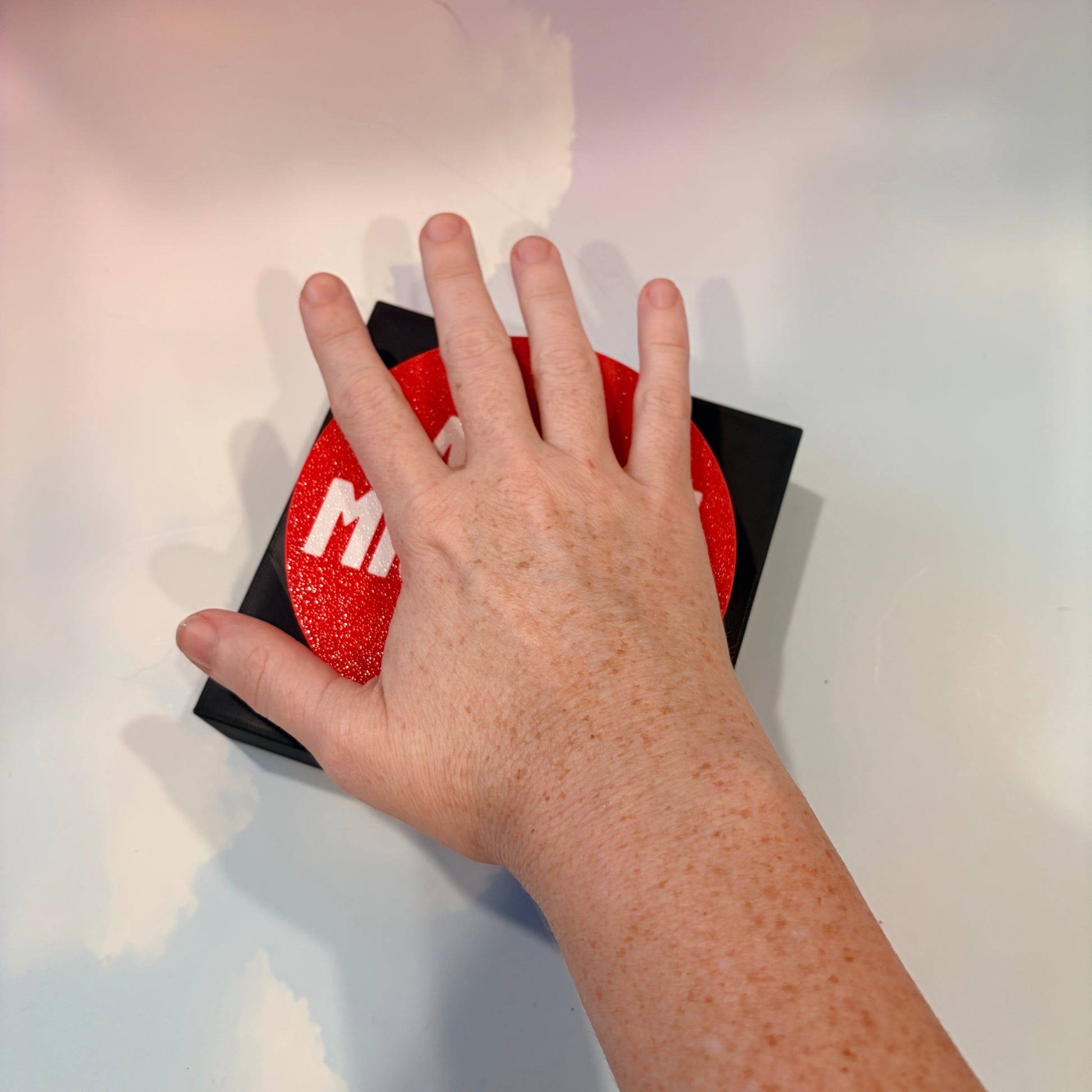 Oversized red 3D printed fidget button with white “LAUNCH MISSILES” lettering on a black square base, shown on a white surface.