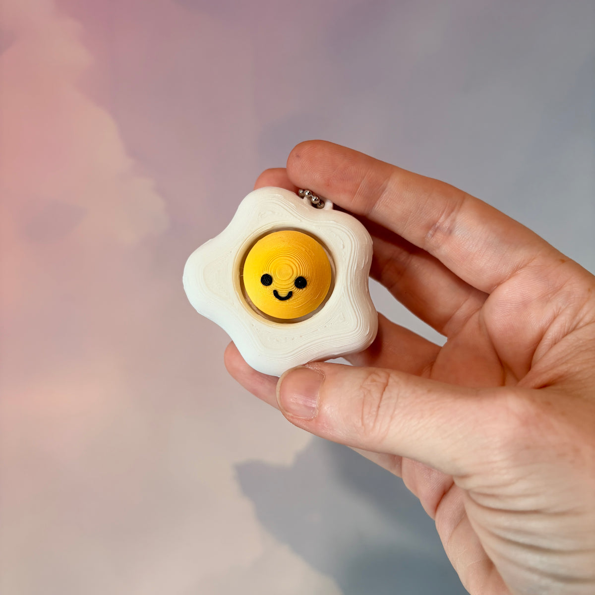 Fried egg shaped fidget clicker toy with a white egg and yellow yolk design, fun food themed desk accessory and satisfying fidget gift.