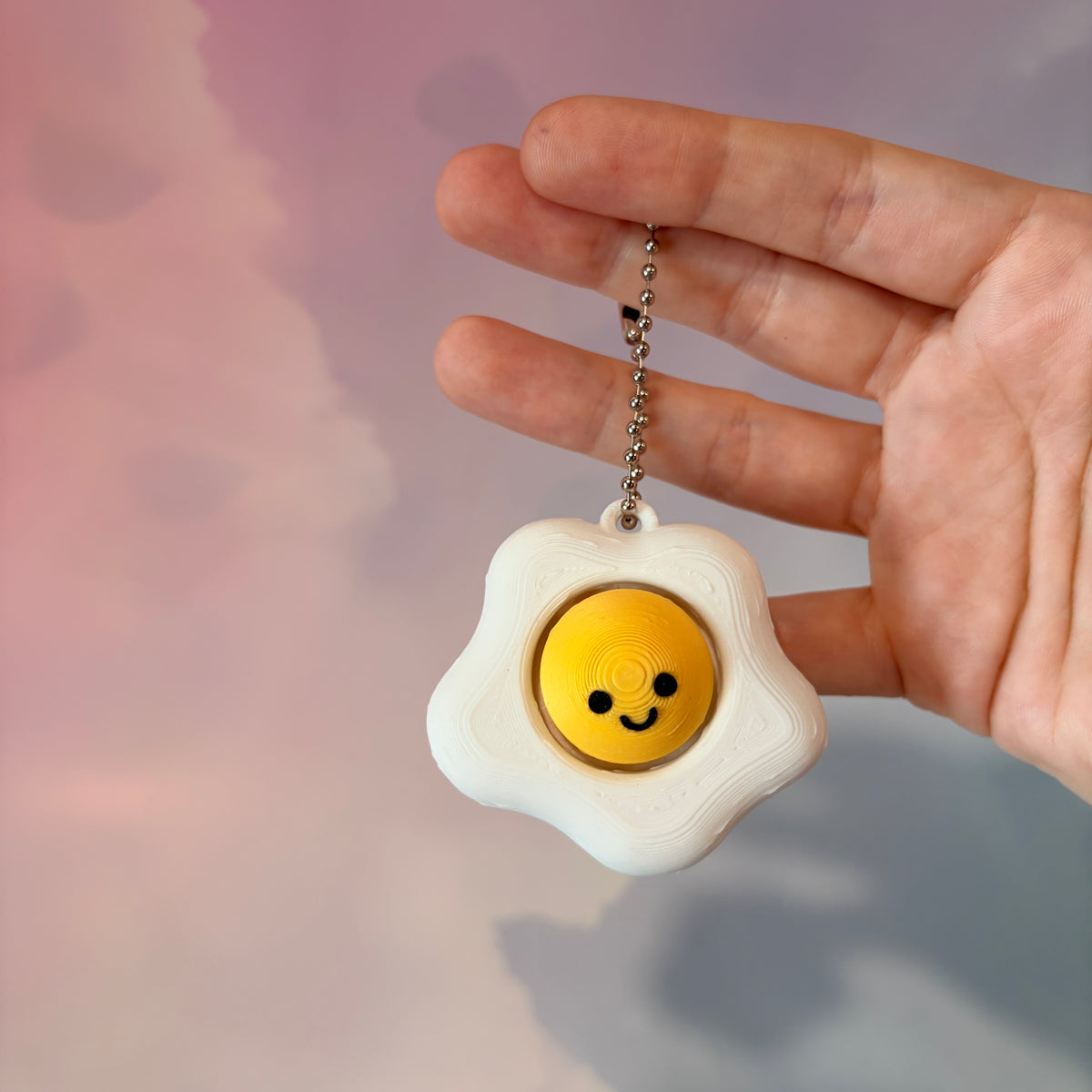 Fried egg shaped fidget clicker toy with a white egg and yellow yolk design, fun food themed desk accessory and satisfying fidget gift.