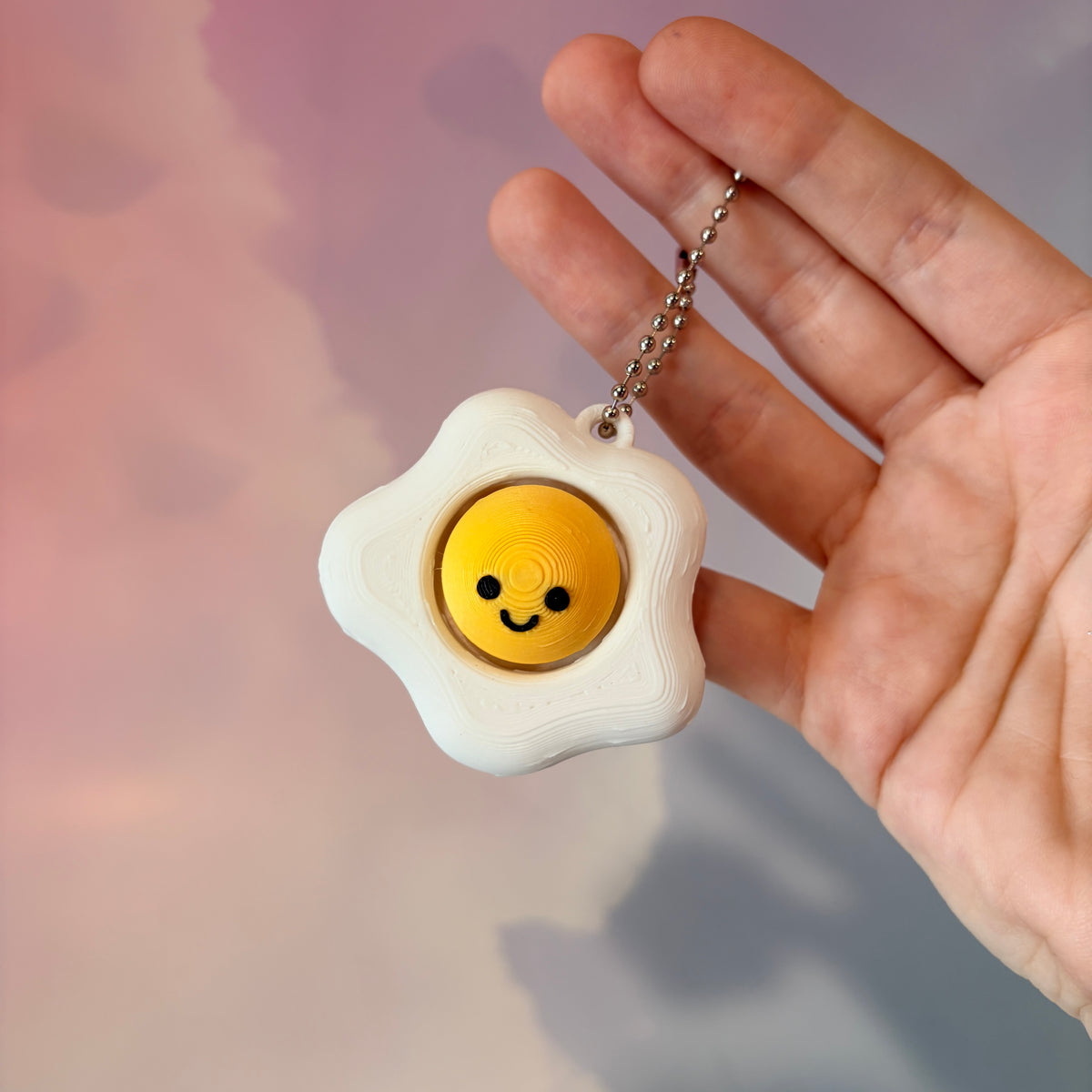 Fried egg shaped fidget clicker toy with a white egg and yellow yolk design, fun food themed desk accessory and satisfying fidget gift.