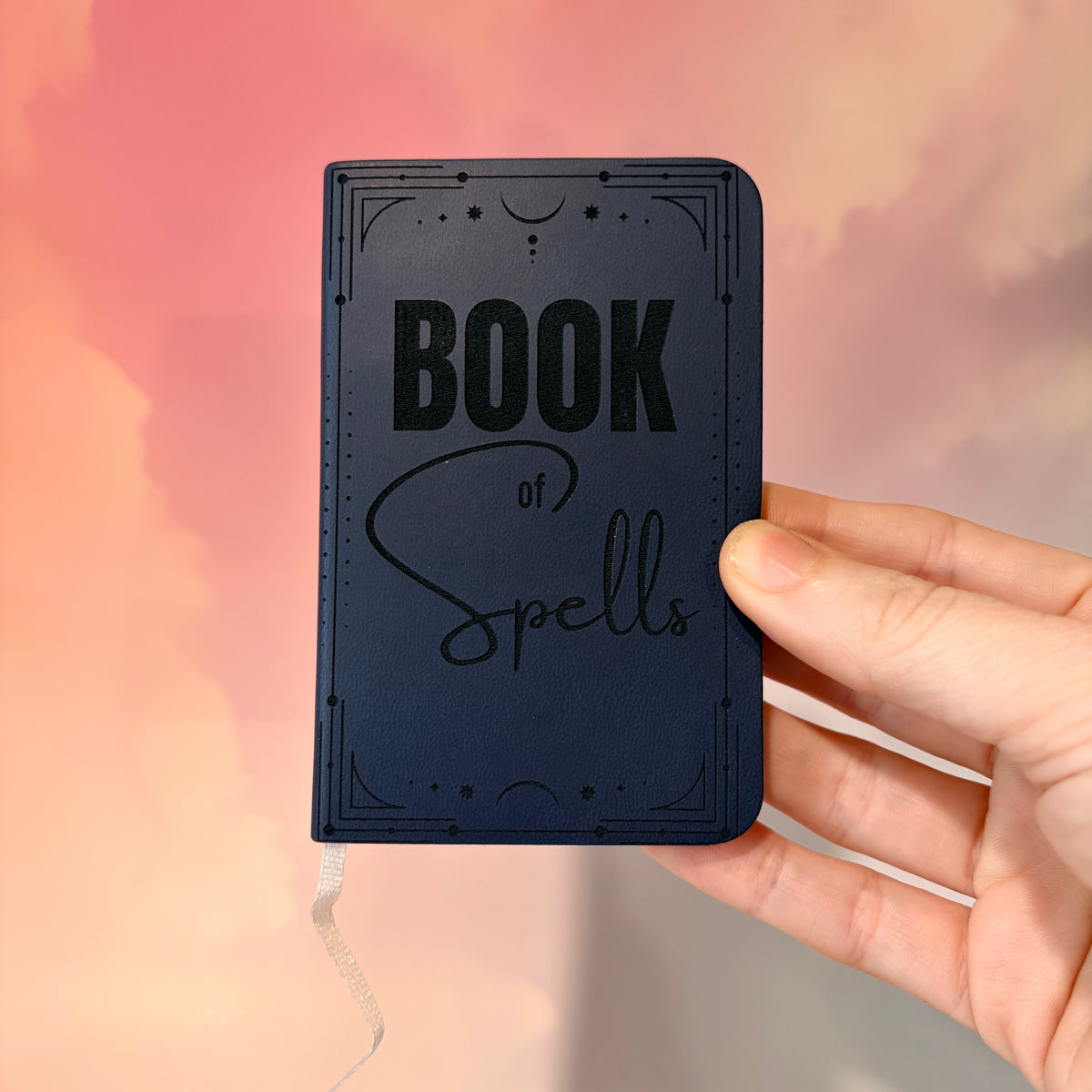 Mini green leather notebook with “Book of Spells” laser engraved on the cover in black lettering. Approximately 4 x 2.5 inches, with 50 lined pages. Available in brown, green, blue, gray, and black.
