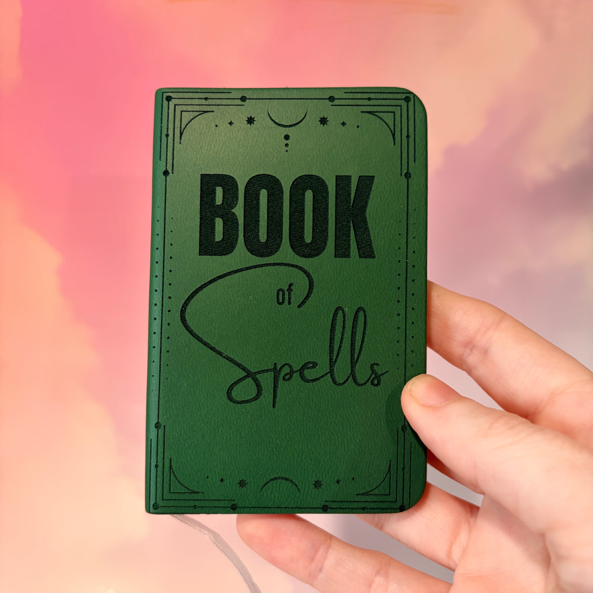 Mini green leather notebook with “Book of Spells” laser engraved on the cover in black lettering. Approximately 4 x 2.5 inches, with 50 lined pages. Available in brown, green, blue, gray, and black.
