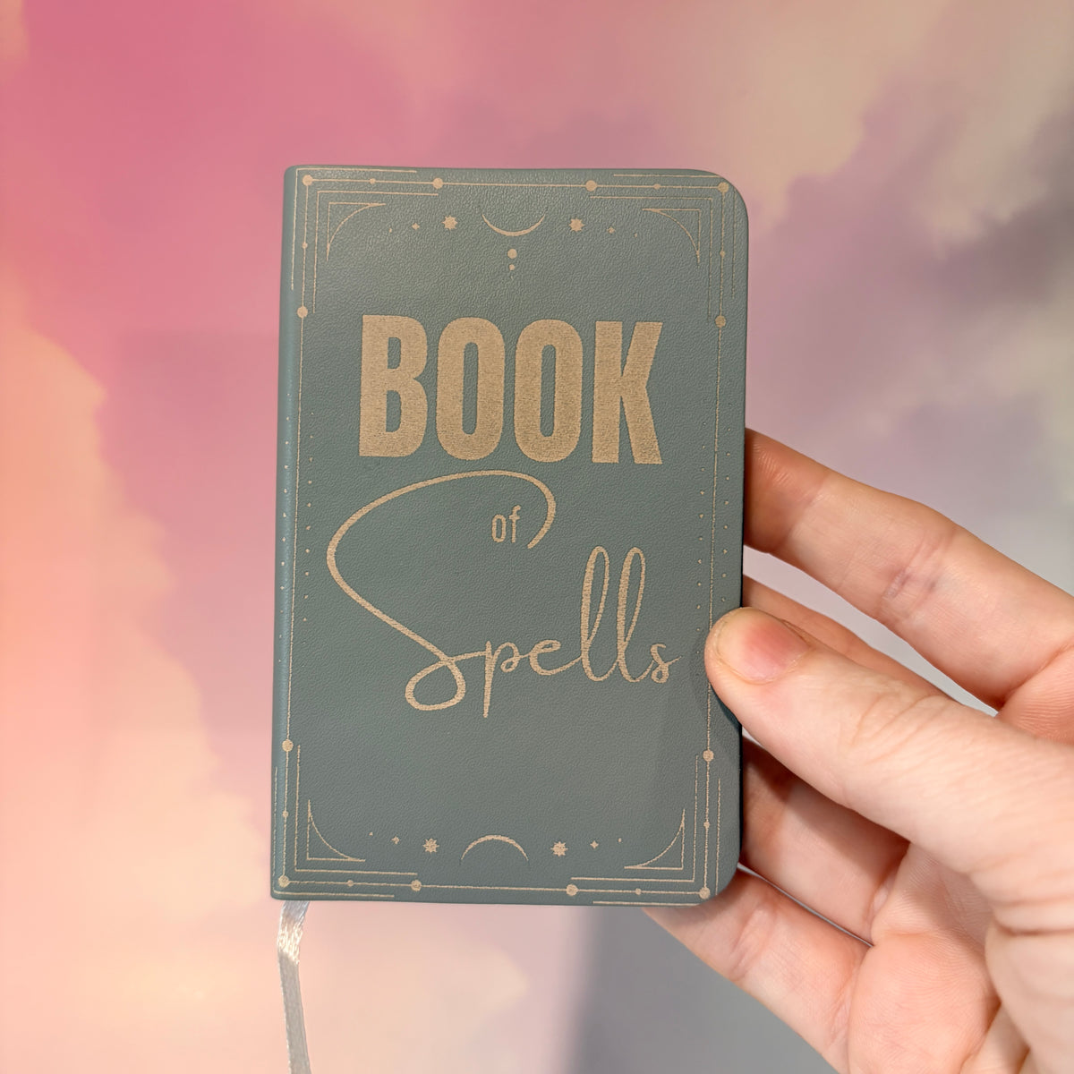 Mini green leather notebook with “Book of Spells” laser engraved on the cover in black lettering. Approximately 4 x 2.5 inches, with 50 lined pages. Available in brown, green, blue, gray, and black.
