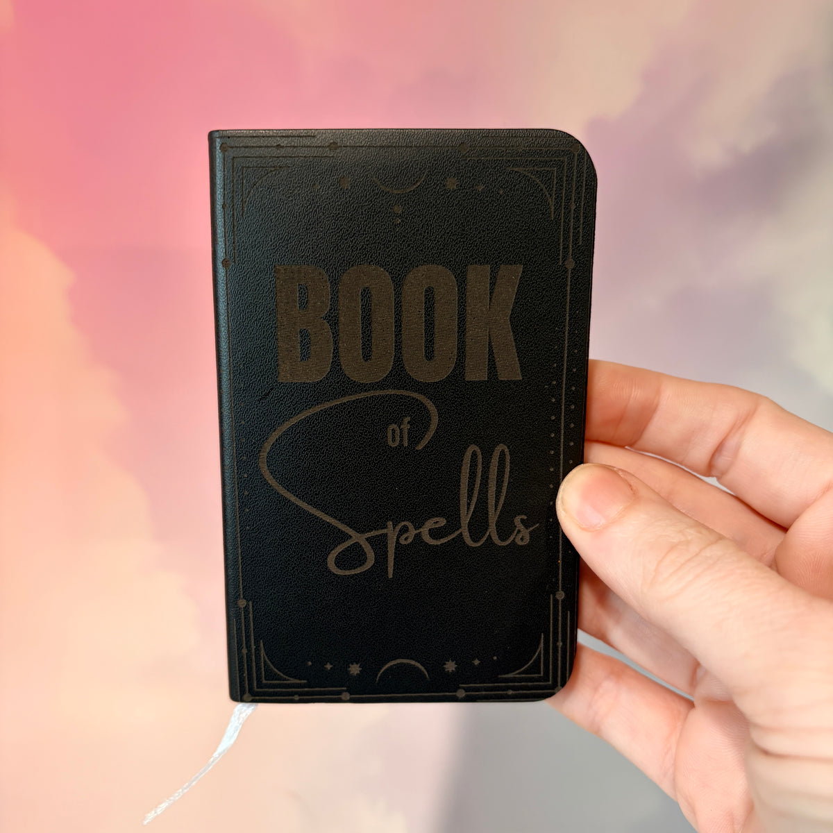 Mini green leather notebook with “Book of Spells” laser engraved on the cover in black lettering. Approximately 4 x 2.5 inches, with 50 lined pages. Available in brown, green, blue, gray, and black.
