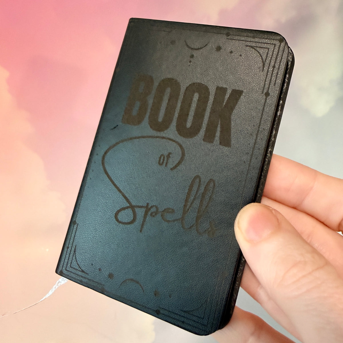 Mini green leather notebook with “Book of Spells” laser engraved on the cover in black lettering. Approximately 4 x 2.5 inches, with 50 lined pages. Available in brown, green, blue, gray, and black.

