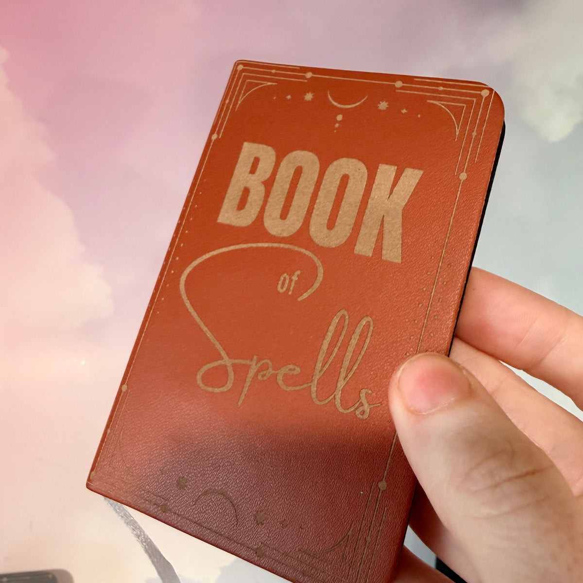 Mini green leather notebook with “Book of Spells” laser engraved on the cover in black lettering. Approximately 4 x 2.5 inches, with 50 lined pages. Available in brown, green, blue, gray, and black.
