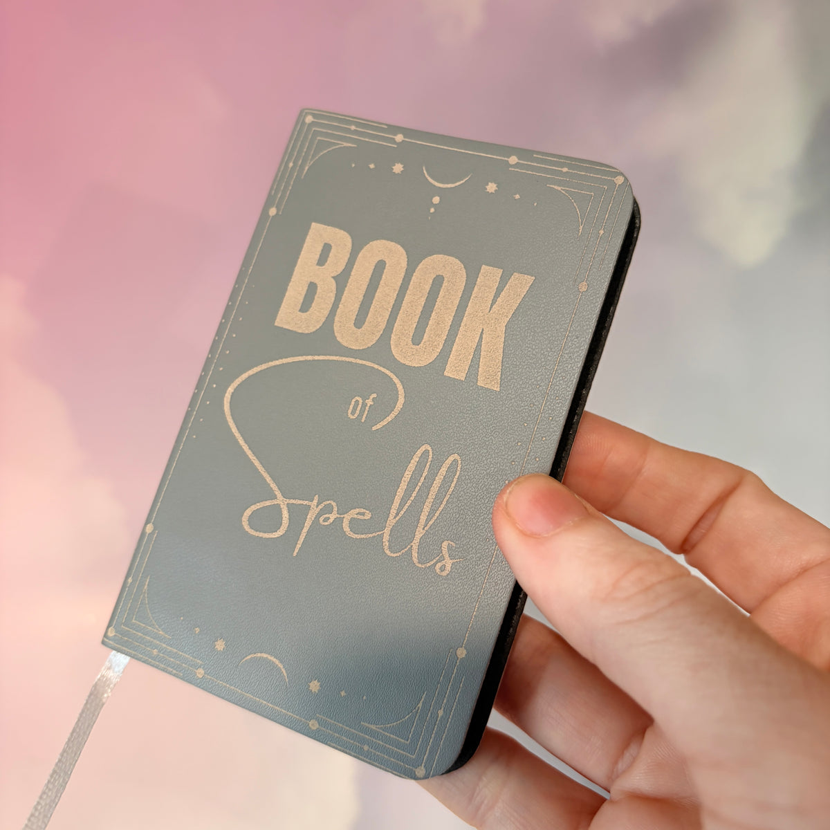 Mini green leather notebook with “Book of Spells” laser engraved on the cover in black lettering. Approximately 4 x 2.5 inches, with 50 lined pages. Available in brown, green, blue, gray, and black.
