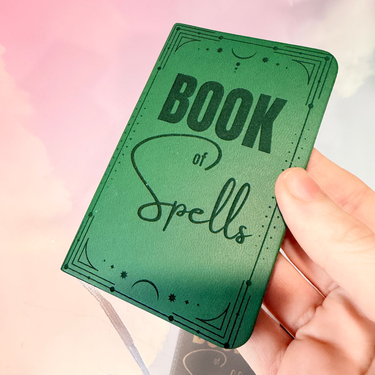 Mini green leather notebook with “Book of Spells” laser engraved on the cover in black lettering. Approximately 4 x 2.5 inches, with 50 lined pages. Available in brown, green, blue, gray, and black.
