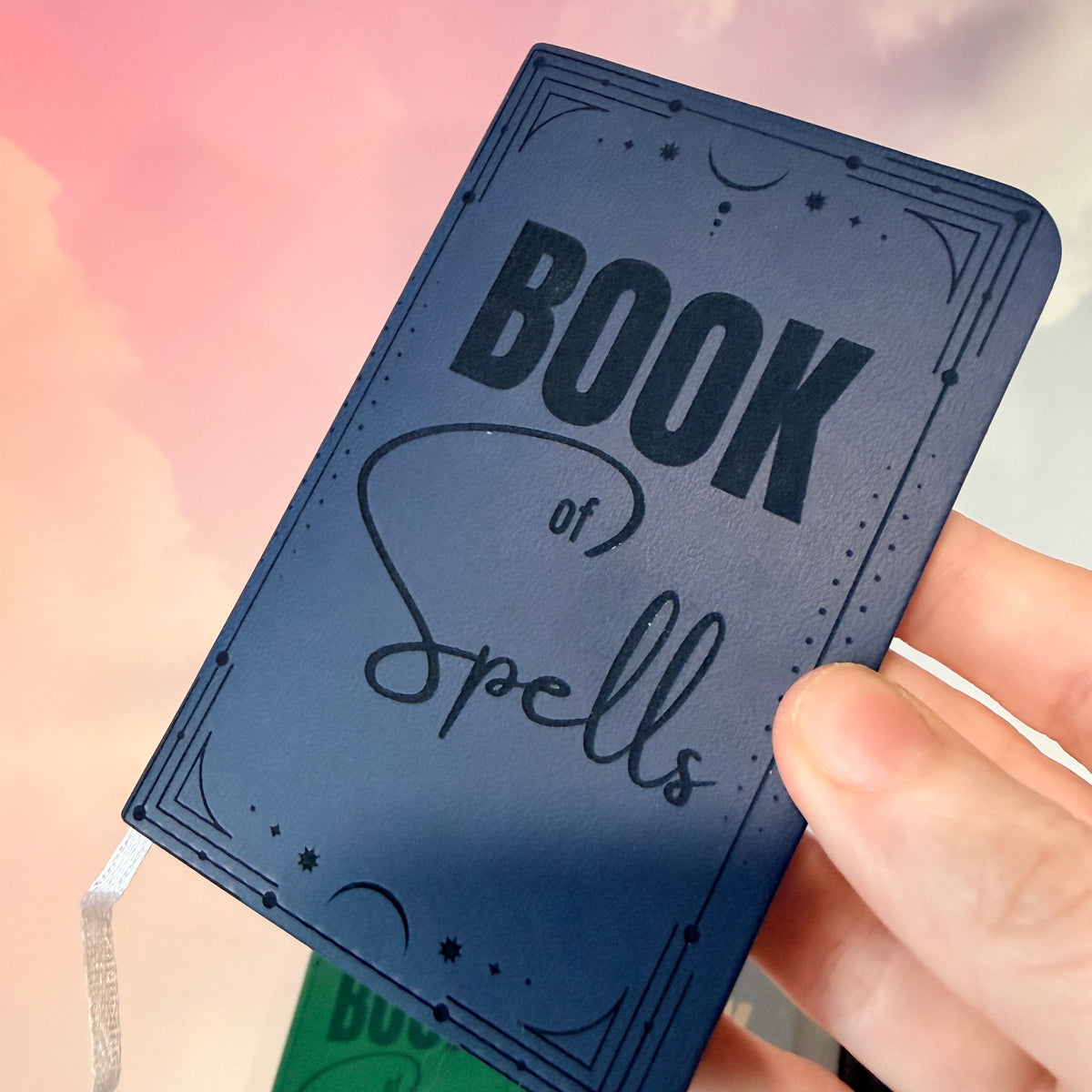 Mini green leather notebook with “Book of Spells” laser engraved on the cover in black lettering. Approximately 4 x 2.5 inches, with 50 lined pages. Available in brown, green, blue, gray, and black.
