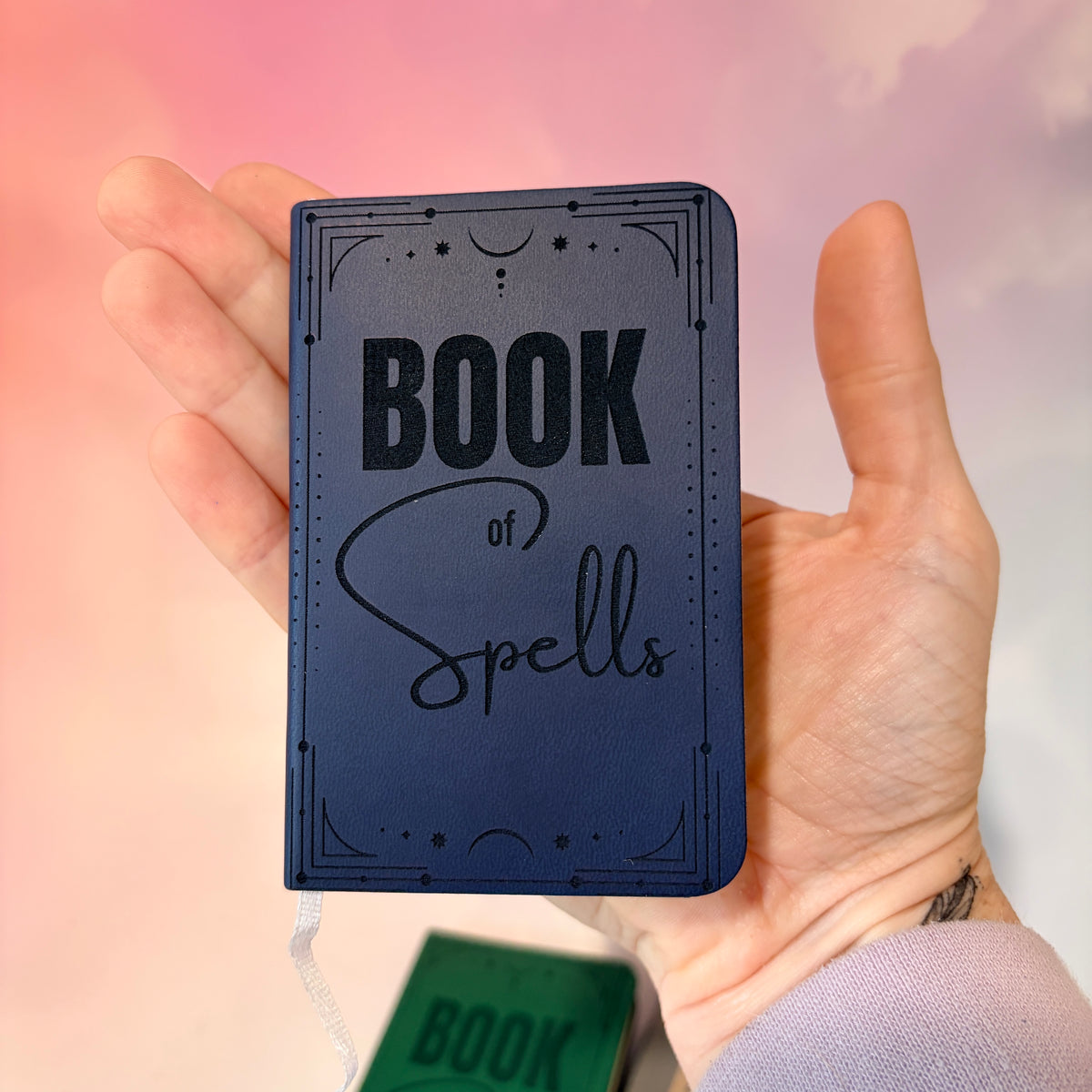 Mini green leather notebook with “Book of Spells” laser engraved on the cover in black lettering. Approximately 4 x 2.5 inches, with 50 lined pages. Available in brown, green, blue, gray, and black.

