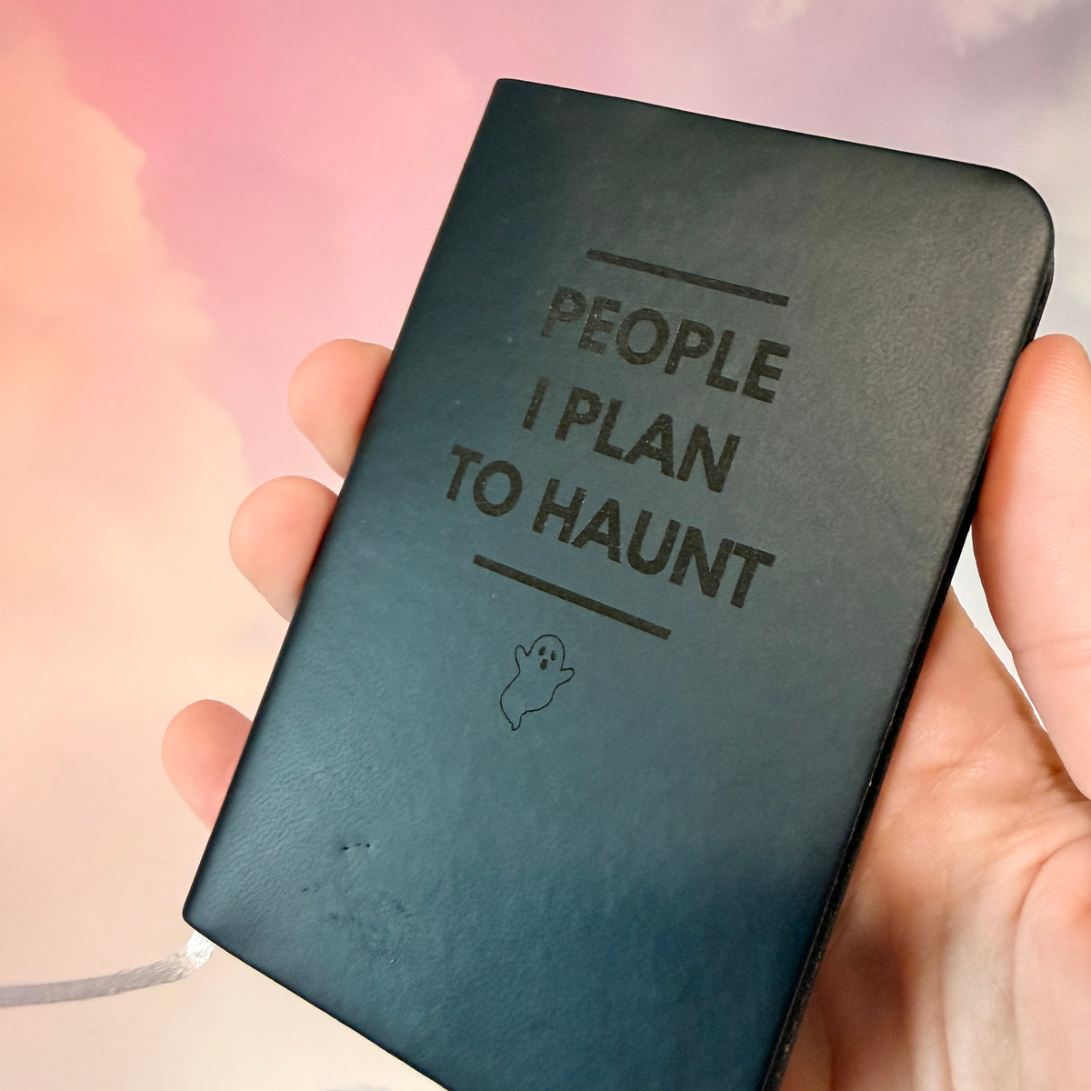 Mini blue notebook with “People I Plan to Haunt” laser engraved in black lettering and a tiny ghost illustration. Approximately 4 x 2.5 inches, with 50 lined pages. Available in brown, green, blue, gray, and black.
