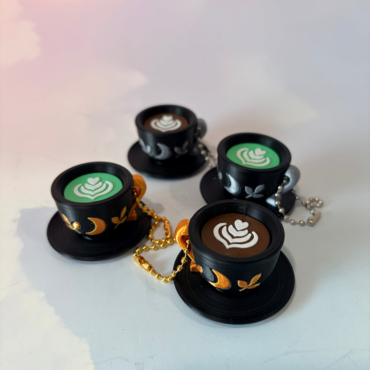 3D printed mystical drink cup fidget clicker keychain with a black floral moon design in gold or silver. Choose matcha or coffee with cute latte art, plus a clicky or silent mechanism.