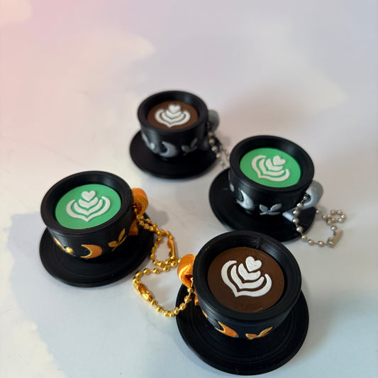 3D printed mystical drink cup fidget clicker keychain with a black floral moon design in gold or silver. Choose matcha or coffee with cute latte art, plus a clicky or silent mechanism.