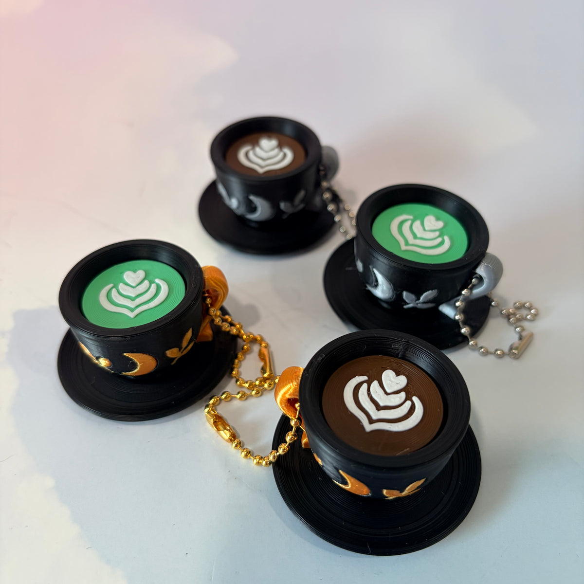3D printed mystical drink cup fidget clicker keychain with a black floral moon design in gold or silver. Choose matcha or coffee with cute latte art, plus a clicky or silent mechanism.