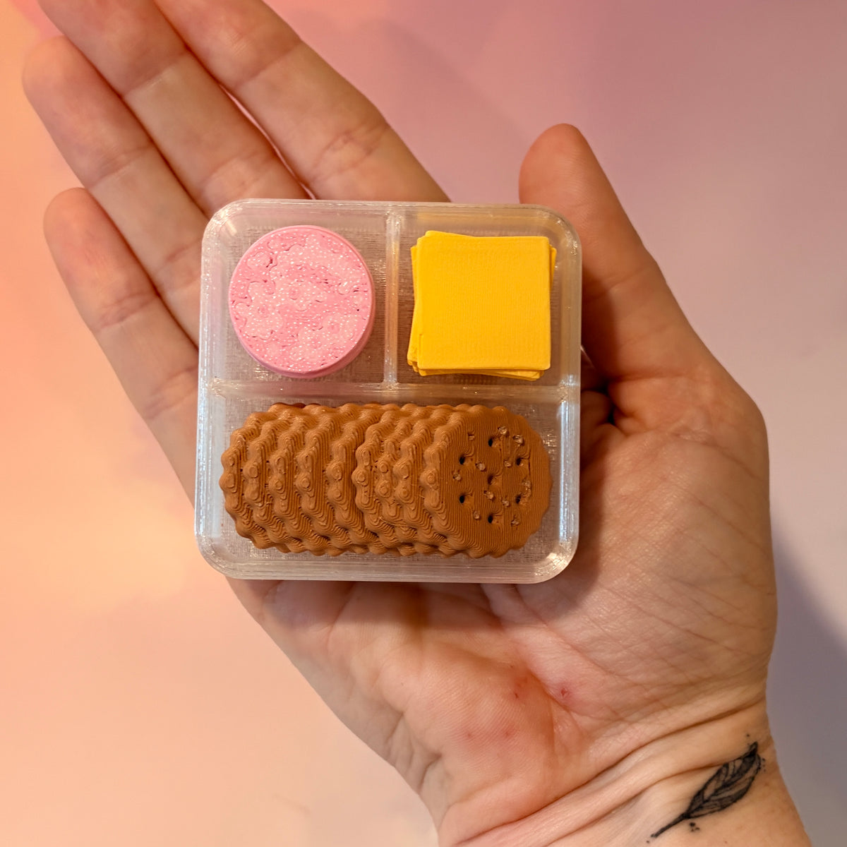 3D printed mini snack box fidget clicker with ham, cheese, and crackers under a semi-transparent lid. Ham and cheese have soft silent presses, while the crackers make satisfying audible clicks.
