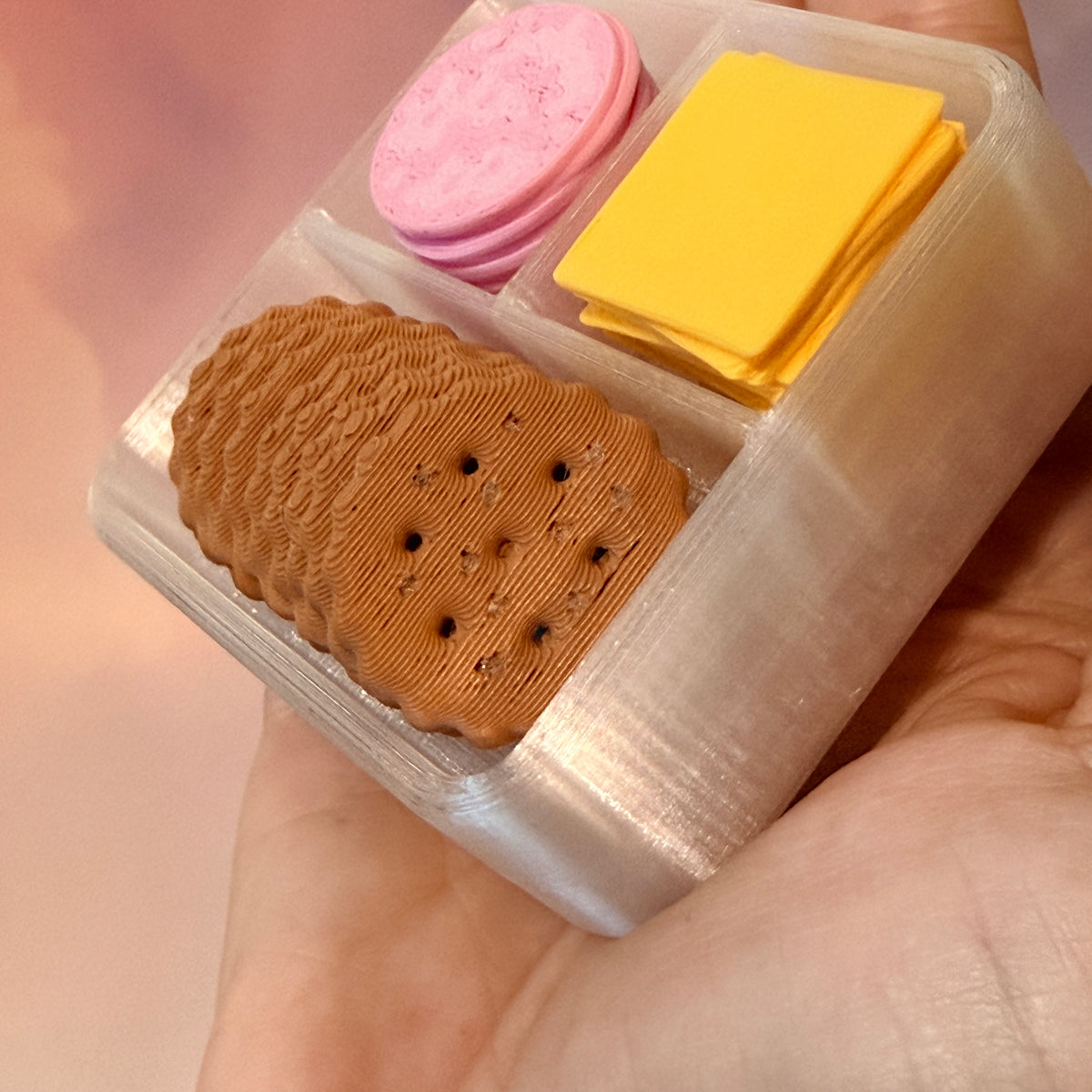 3D printed mini snack box fidget clicker with ham, cheese, and crackers under a semi-transparent lid. Ham and cheese have soft silent presses, while the crackers make satisfying audible clicks.