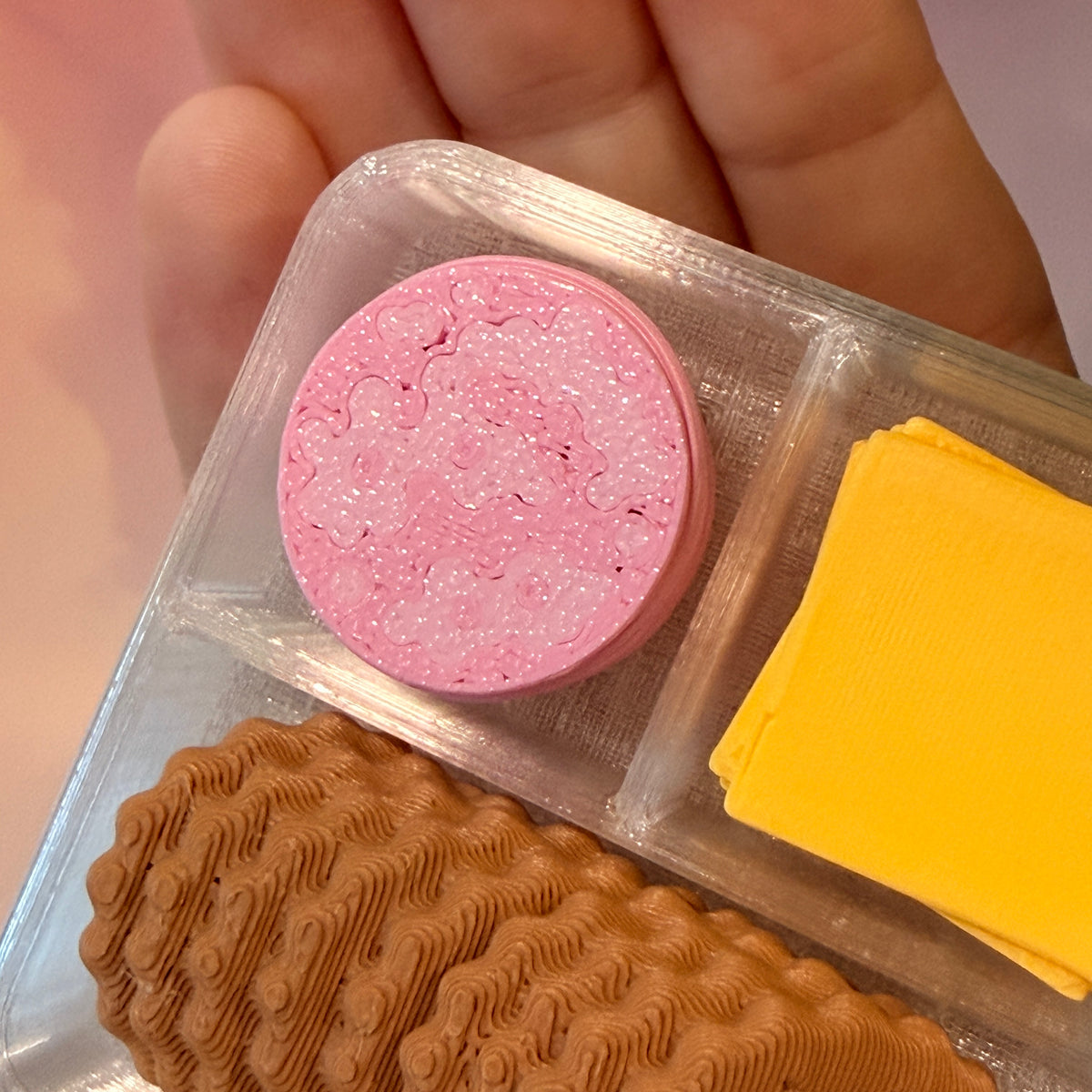 3D printed mini snack box fidget clicker with ham, cheese, and crackers under a semi-transparent lid. Ham and cheese have soft silent presses, while the crackers make satisfying audible clicks.