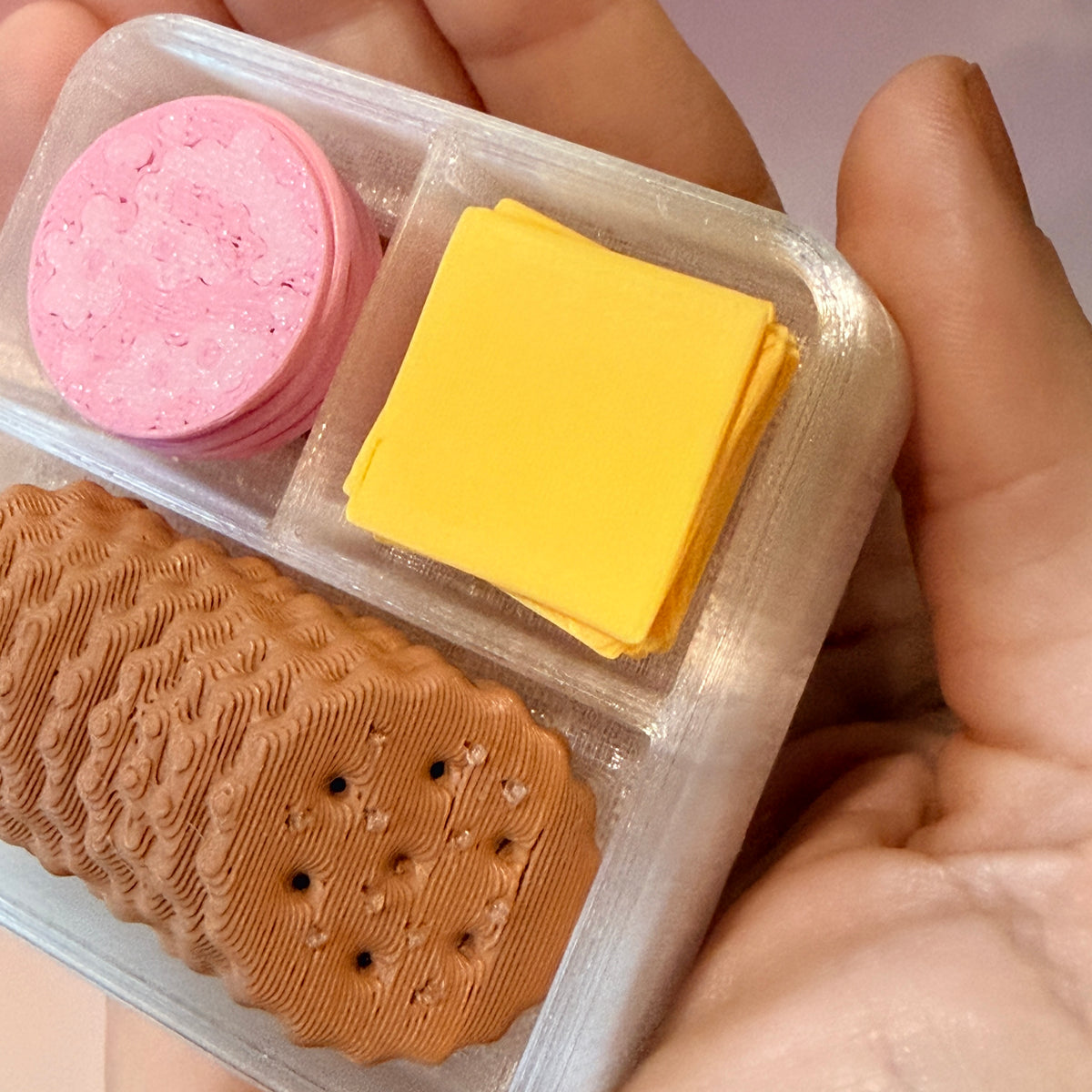 3D printed mini snack box fidget clicker with ham, cheese, and crackers under a semi-transparent lid. Ham and cheese have soft silent presses, while the crackers make satisfying audible clicks.