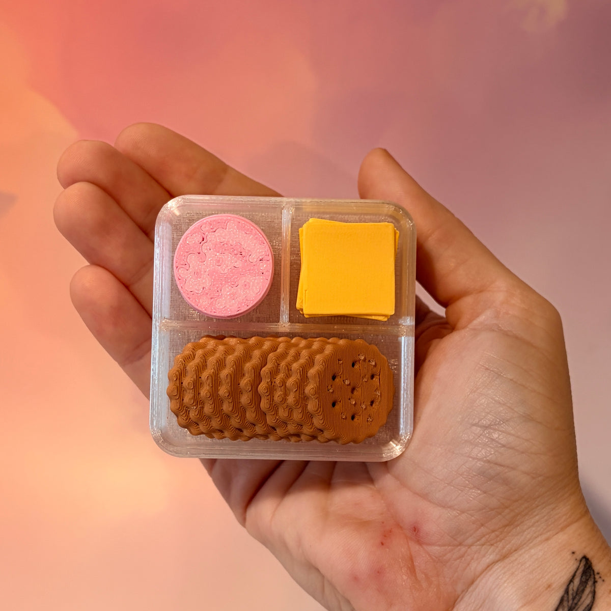 3D printed mini snack box fidget clicker with ham, cheese, and crackers under a semi-transparent lid. Ham and cheese have soft silent presses, while the crackers make satisfying audible clicks.
