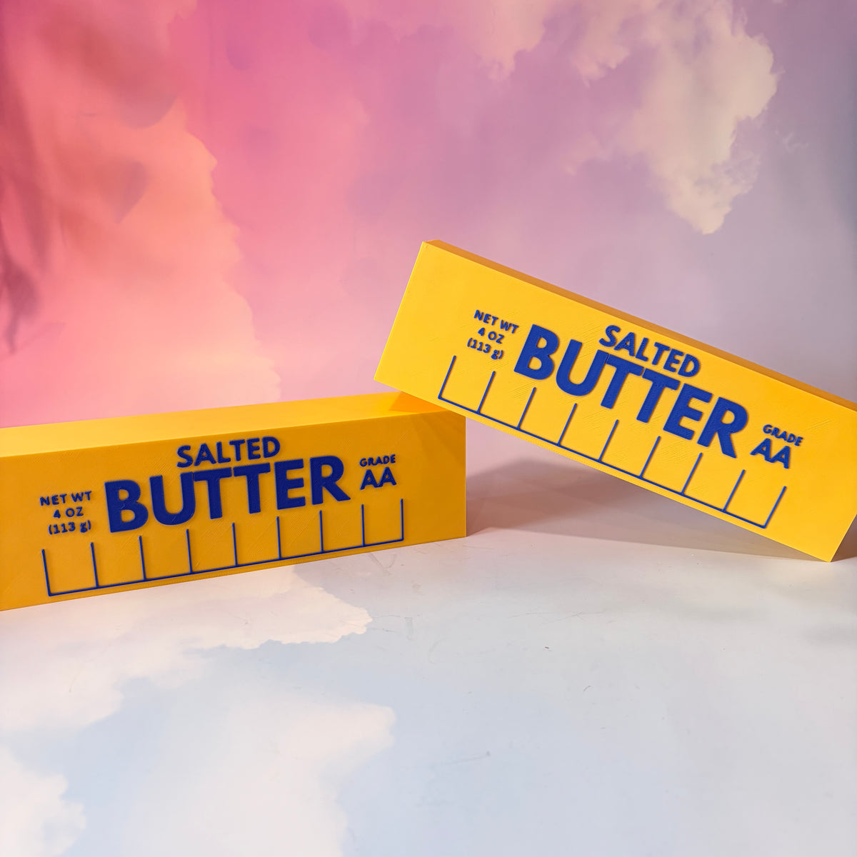 Oversized 3D printed novelty stick of butter, approximately 8.5 inches long, featuring classic tablespoon measurement lines, Grade AA labeling, and net weight details. Whimsical food-themed decor for kitchens and farmhouse-style homes.