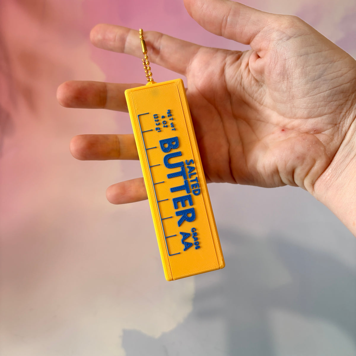 3D printed stick of butter bag charm with gold hardware, classic TBSP markings, Grade AA label, and net weight details. Sliding top hides a lipstick or chapstick in a magnetic compartment.