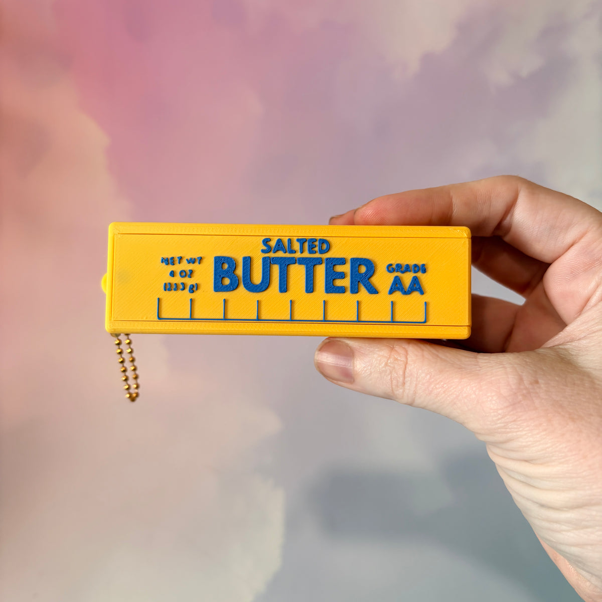 3D printed stick of butter bag charm with gold hardware, classic TBSP markings, Grade AA label, and net weight details. Sliding top hides a lipstick or chapstick in a magnetic compartment.