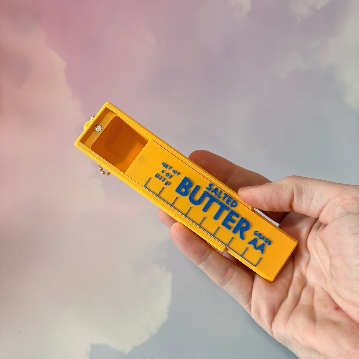 3D printed stick of butter bag charm with gold hardware, classic TBSP markings, Grade AA label, and net weight details. Sliding top hides a lipstick or chapstick in a magnetic compartment.