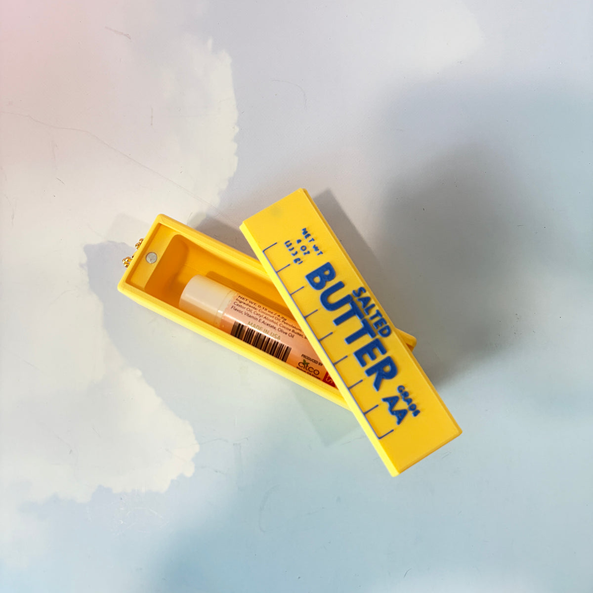 3D printed stick of butter bag charm with gold hardware, classic TBSP markings, Grade AA label, and net weight details. Sliding top hides a lipstick or chapstick in a magnetic compartment.
