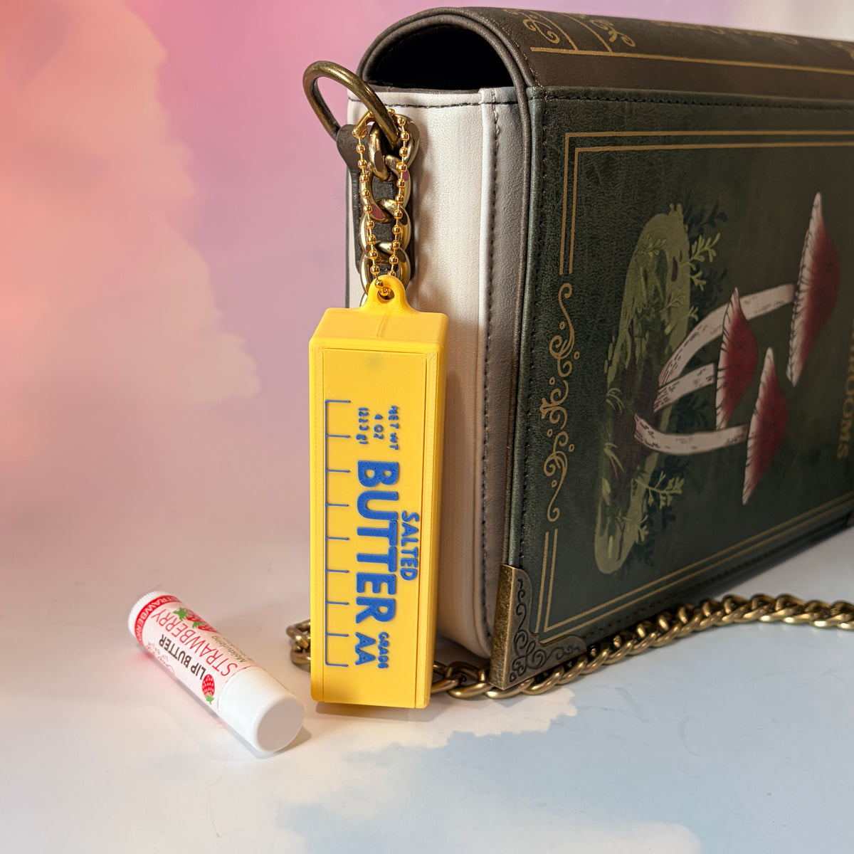 3D printed stick of butter bag charm with gold hardware, classic TBSP markings, Grade AA label, and net weight details. Sliding top hides a lipstick or chapstick in a magnetic compartment.