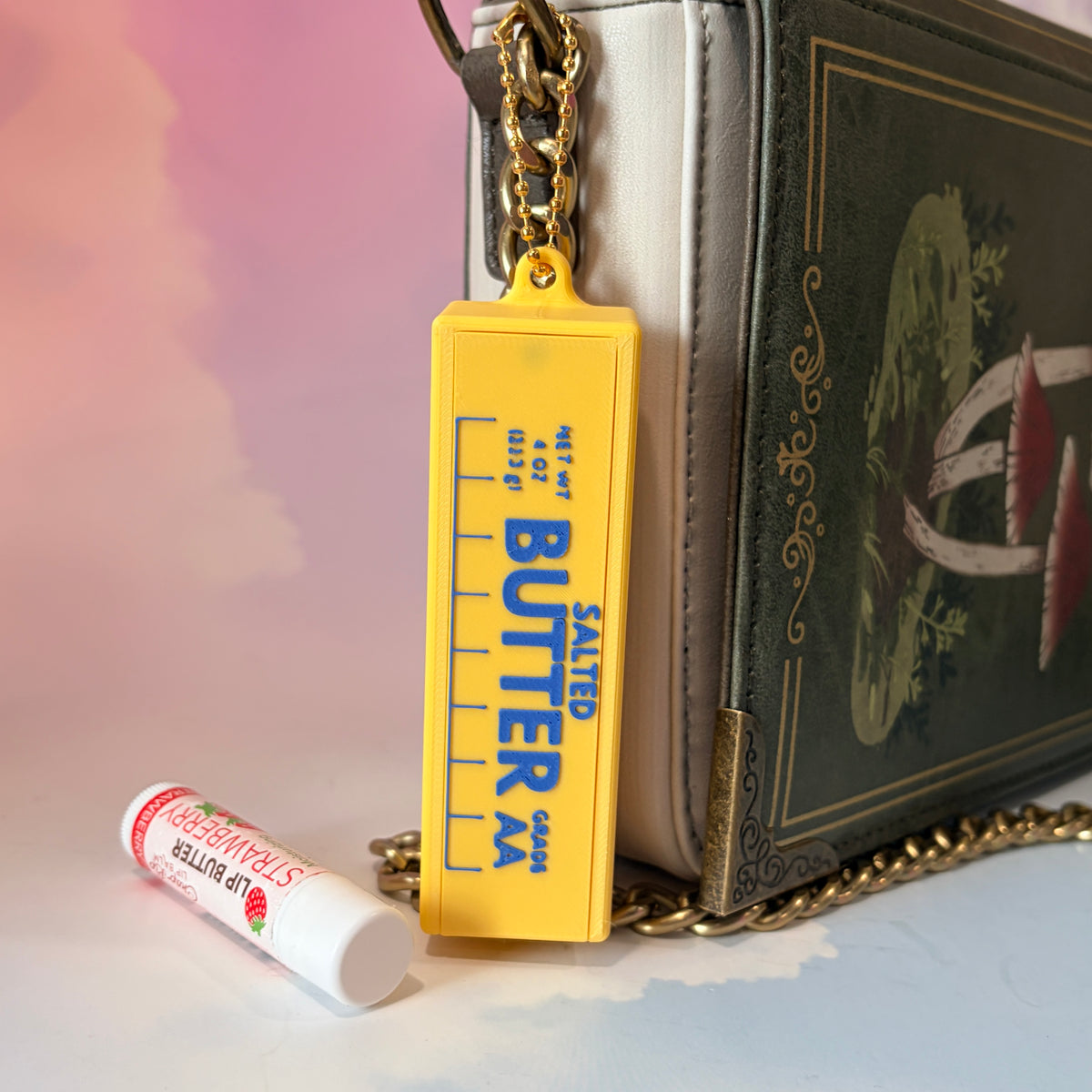 3D printed stick of butter bag charm with gold hardware, classic TBSP markings, Grade AA label, and net weight details. Sliding top hides a lipstick or chapstick in a magnetic compartment.