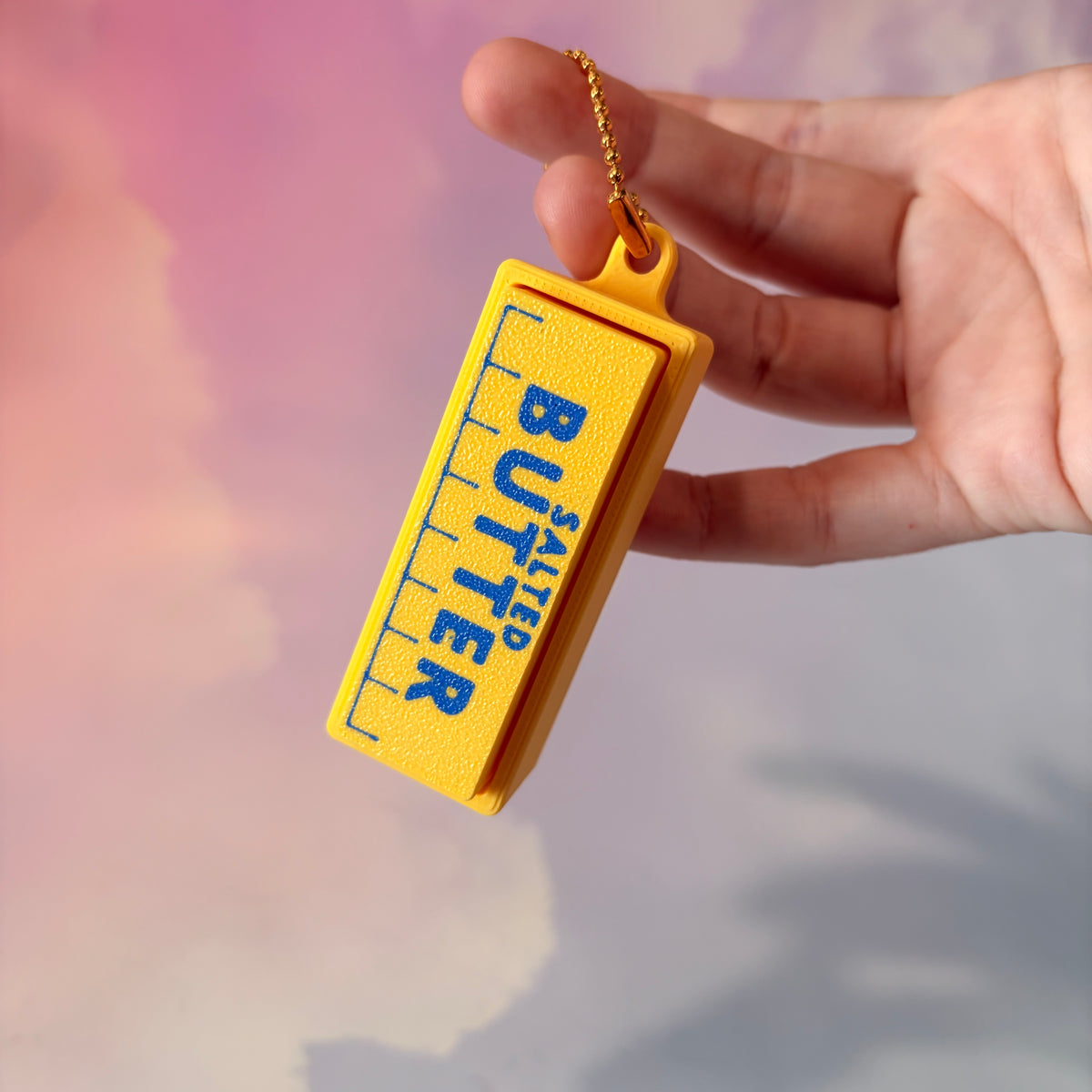 3D printed stick of butter fidget clicker keychain with classic tablespoon marking lines, gold-tone hardware, and two satisfying clicky key switches, perfect for foodies and whimsical accessory lovers.