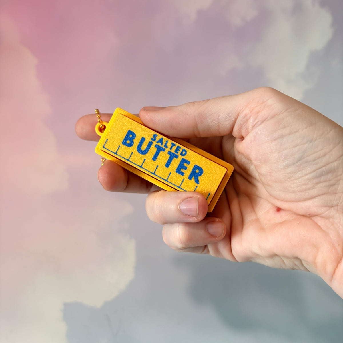 3D printed stick of butter fidget clicker keychain with classic tablespoon marking lines, gold-tone hardware, and two satisfying clicky key switches, perfect for foodies and whimsical accessory lovers.