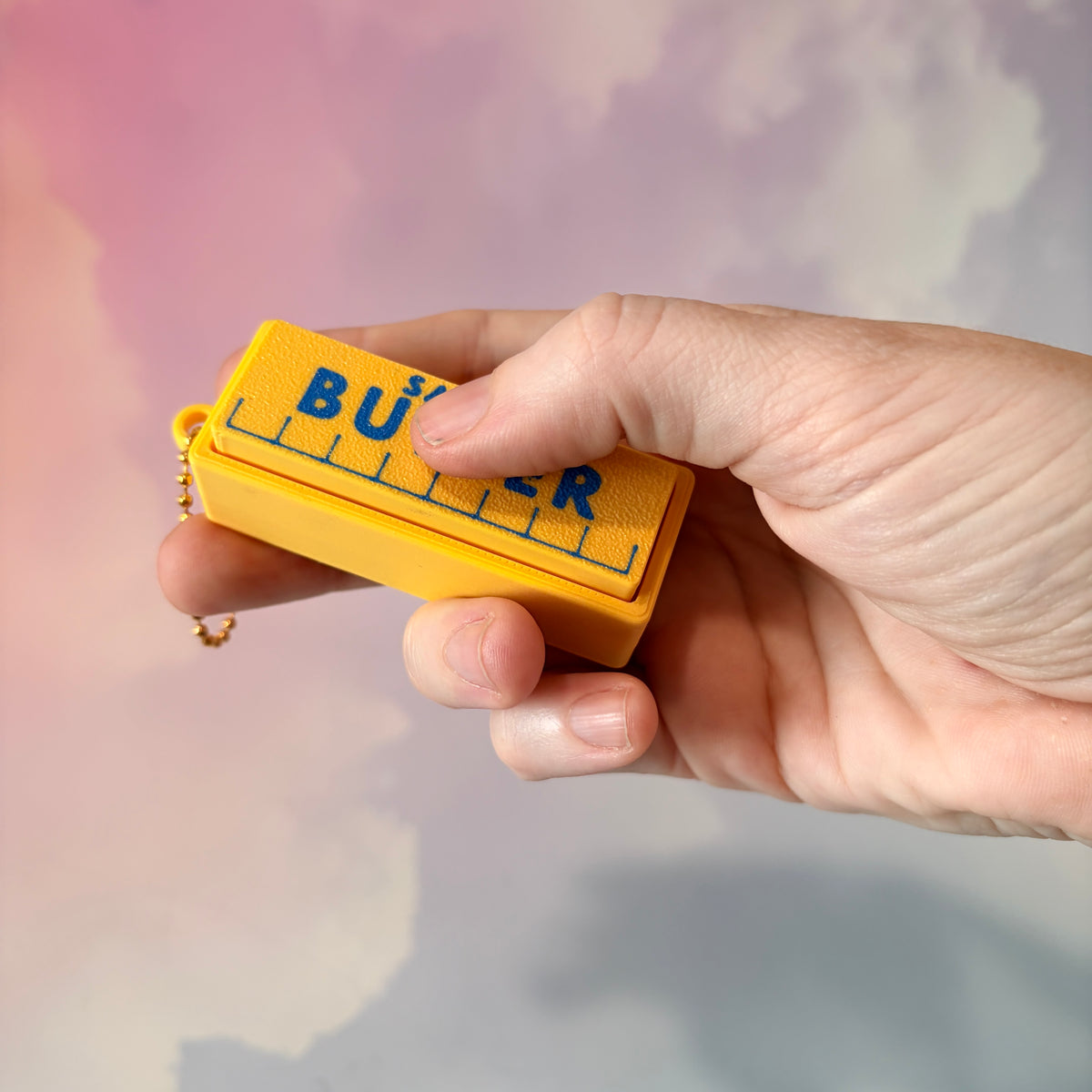 3D printed stick of butter fidget clicker keychain with classic tablespoon marking lines, gold-tone hardware, and two satisfying clicky key switches, perfect for foodies and whimsical accessory lovers.